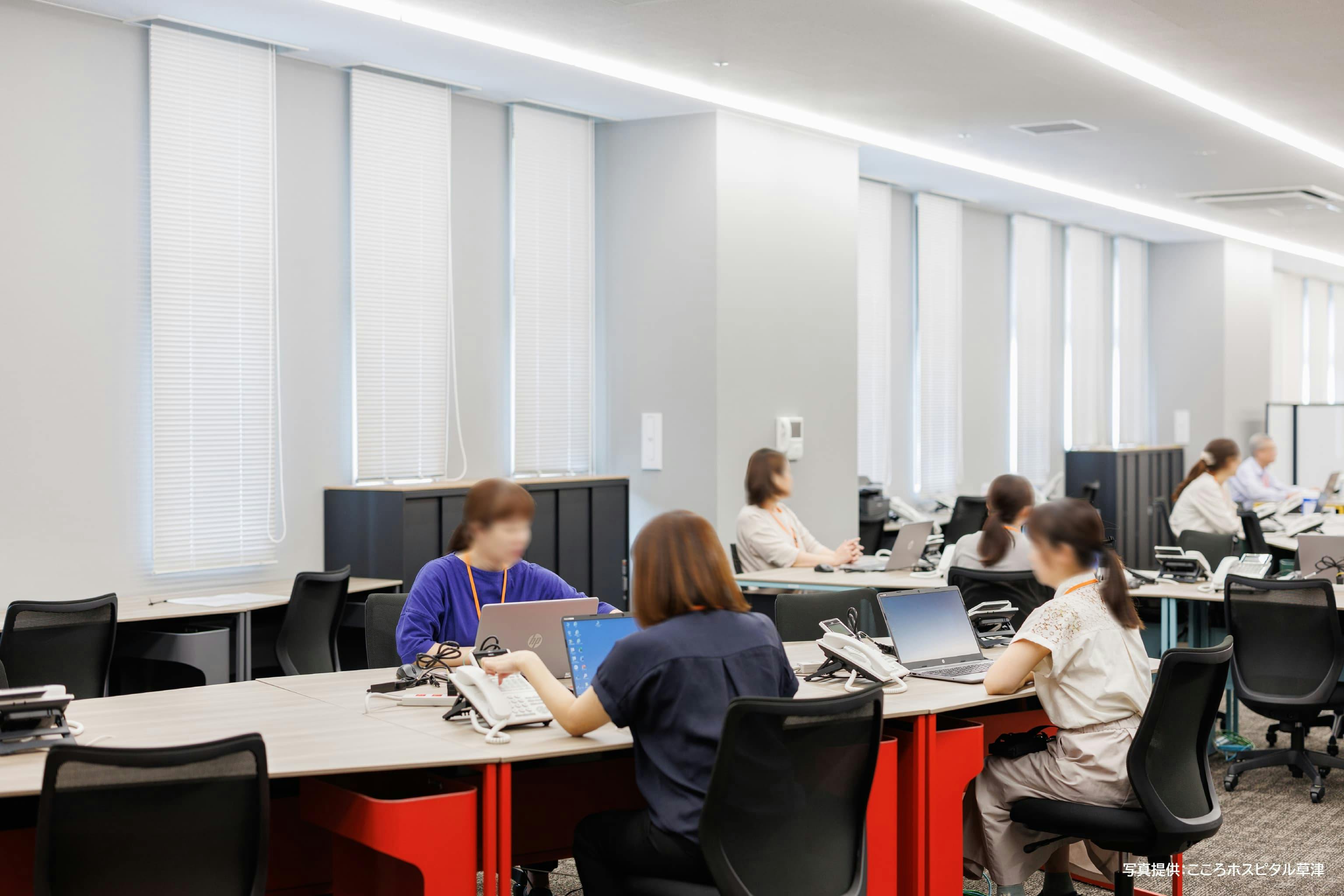 医療法人社団 更生会　こころホスピタル草津 様の事例写真／[3F地域支援センター]イスや棚の扉、カーペットは黒やグレーの落ち着いたトーンでまとめて、集中しやすい空間に。机の脚に使われている赤・黄・緑・青のカラフルな差し色が、働く人たちの気分を明るくしてくれます。