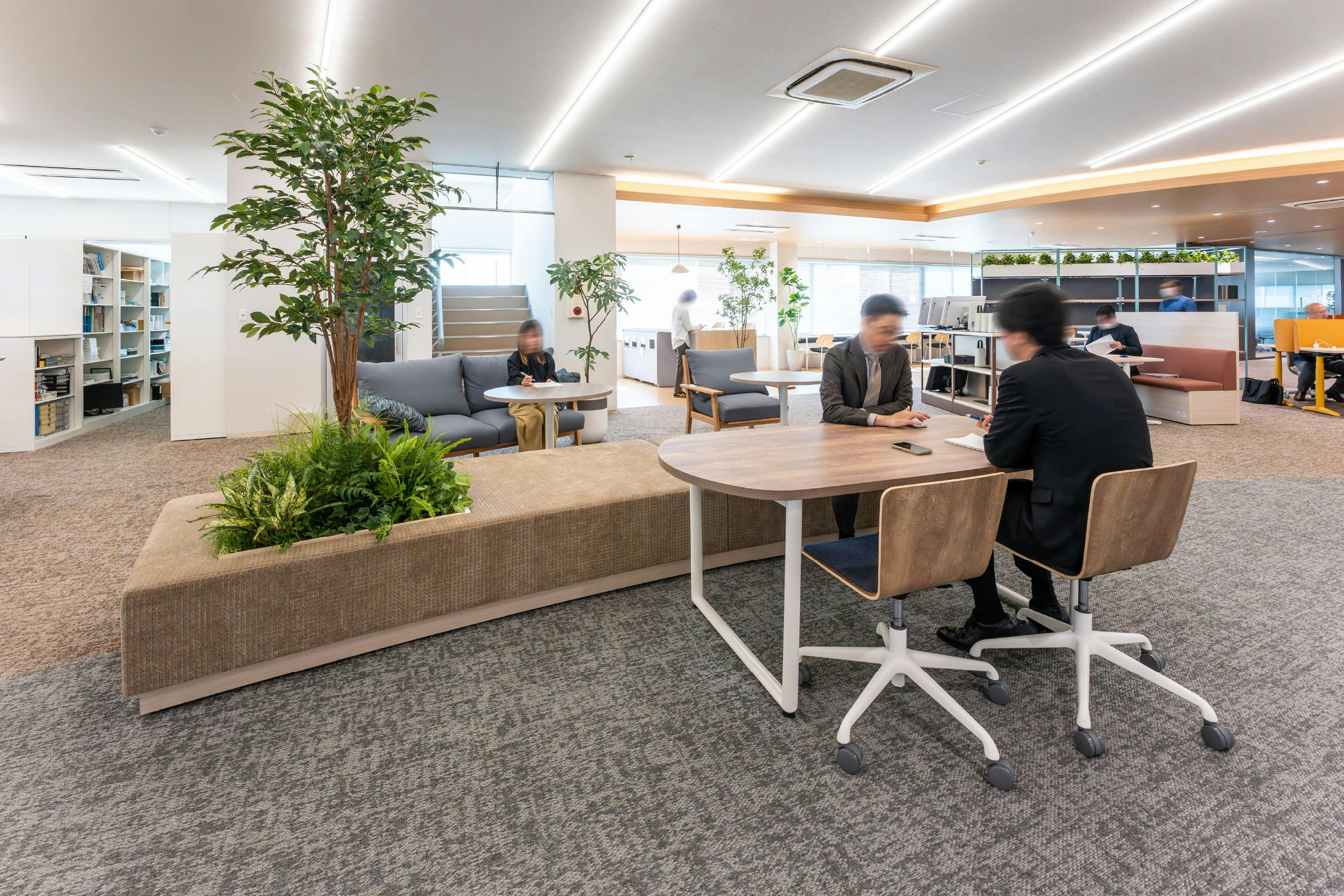 株式会社清永宇蔵商店 様の事例写真／[打ち合わせスペース]フロア中央には、フェイクグリーンを埋め込んだ造作ソファを配置。その一角にテーブルとチェアが置かれています。適度にリラックスできるエリアがあることで、「少し話そうか」と声がかけやすくなったと評判です。
