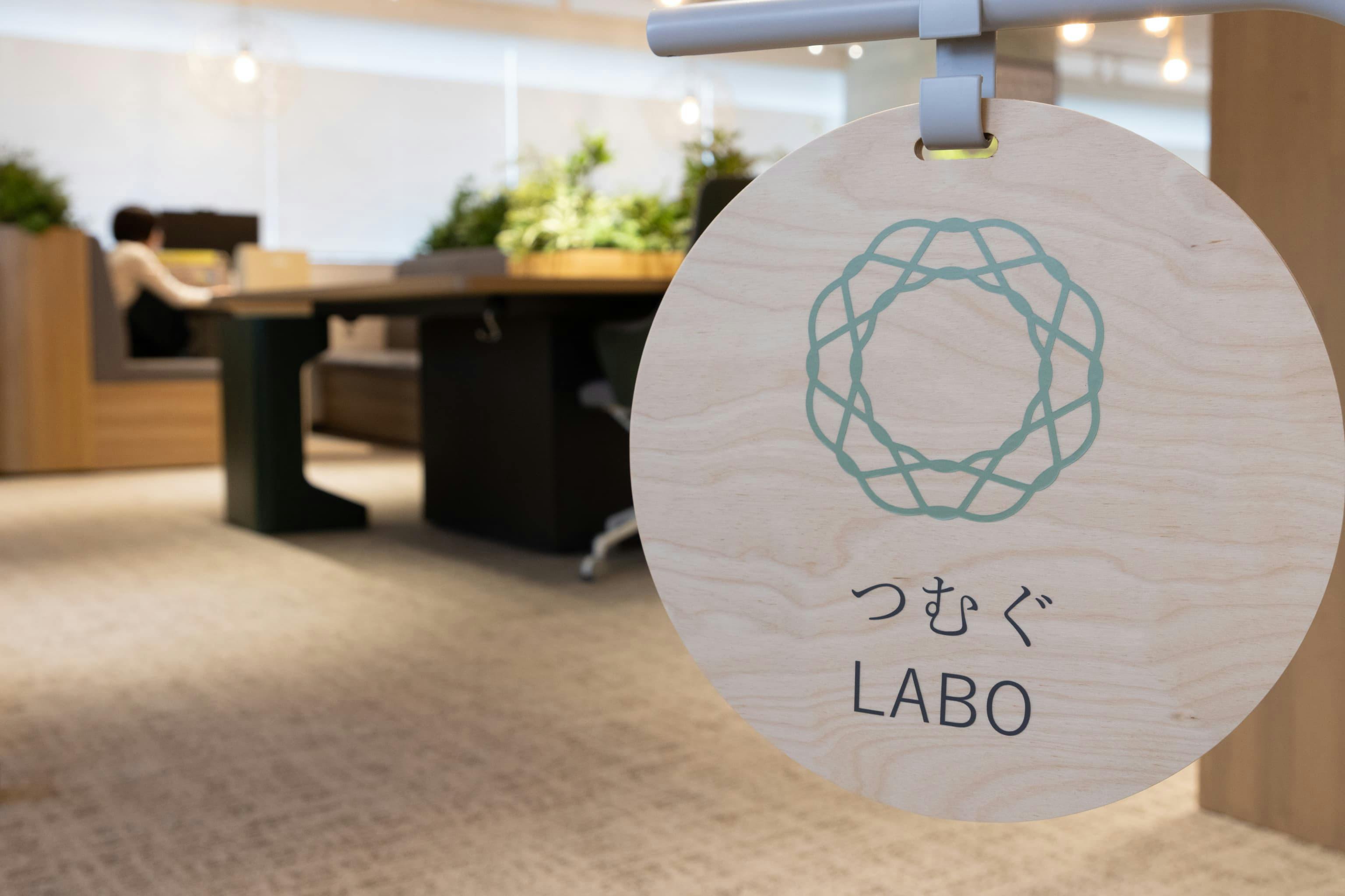 株式会社オカムラ 群馬ラボオフィス『つむぐLABO』の事例写真／[エントランスの看板]「つむぐ」は群馬の地域性と、社員や来訪者の多様な個性を重ね合わせたデザインコンセプト。実際に働く中で気づきを得られるラボオフィスとして、日々、空間と働き方のアップデートが続けられています。