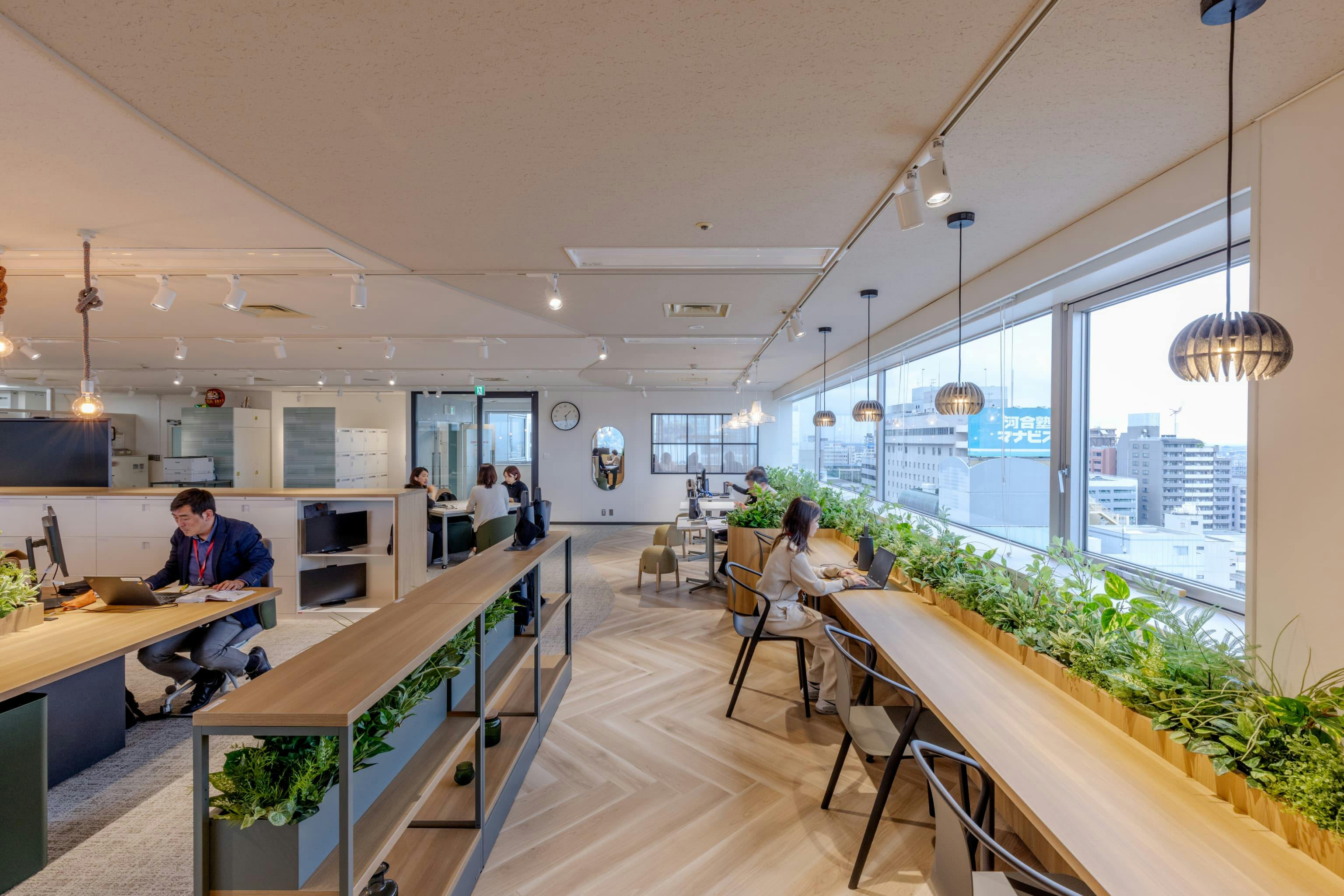 株式会社オカムラ 群馬ラボオフィス『つむぐLABO』の事例写真／[カフェエリア]床の貼り分けと抜け感のある棚で、エリアをゆるやかにゾーニング。窓際のプランターボックス下部は収納スペースになっており、防災グッズが保管されています。美観を損なわず、使いやすさも考えられた工夫です。