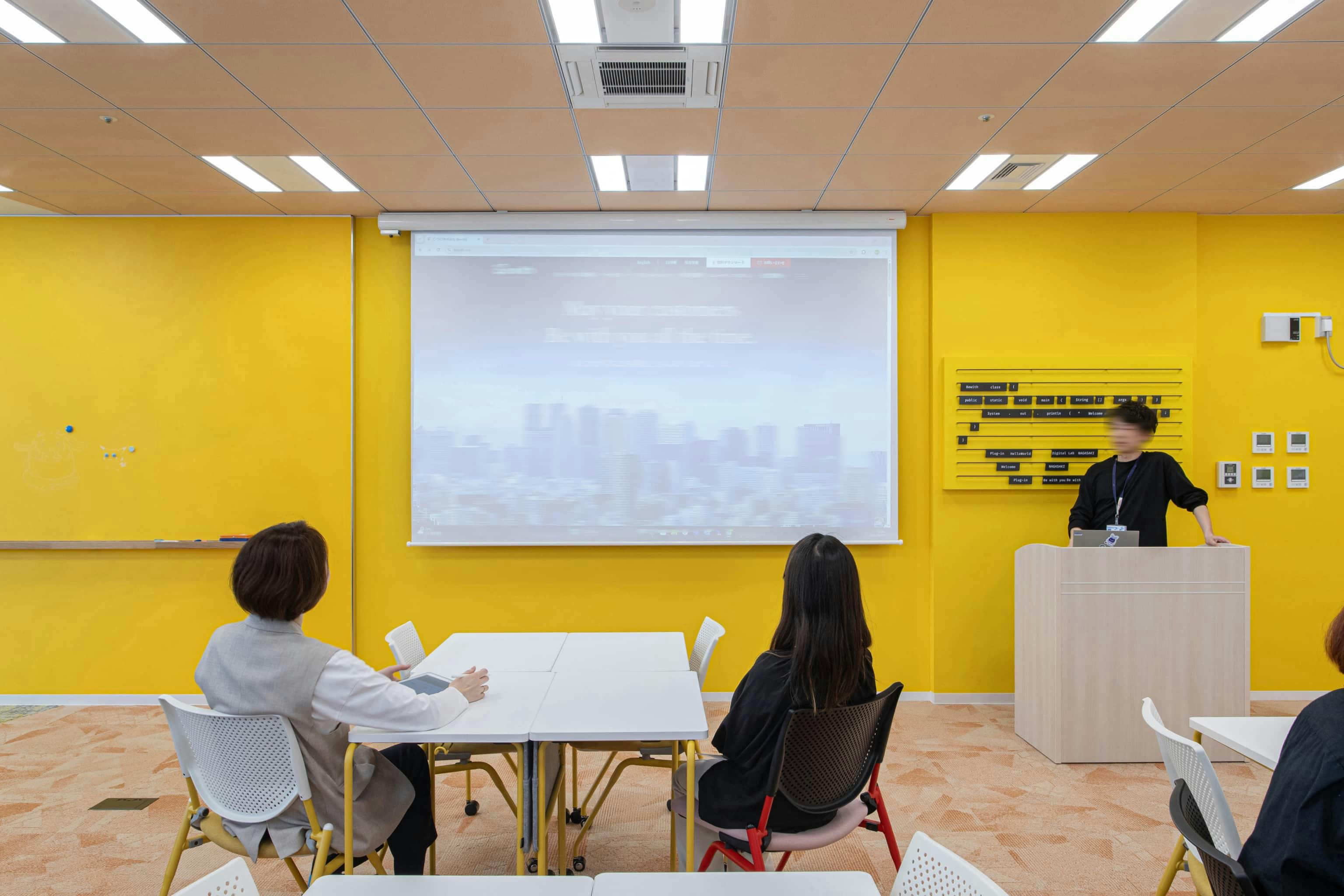 ビーウィズ株式会社 様の事例写真／[共創エリア]プロジェクターと演台が設置され、アイデアを出し合う交流会や技術開発セミナーが開催されています。知識や技術を共有し、みんなで成長できる環境が整っています。