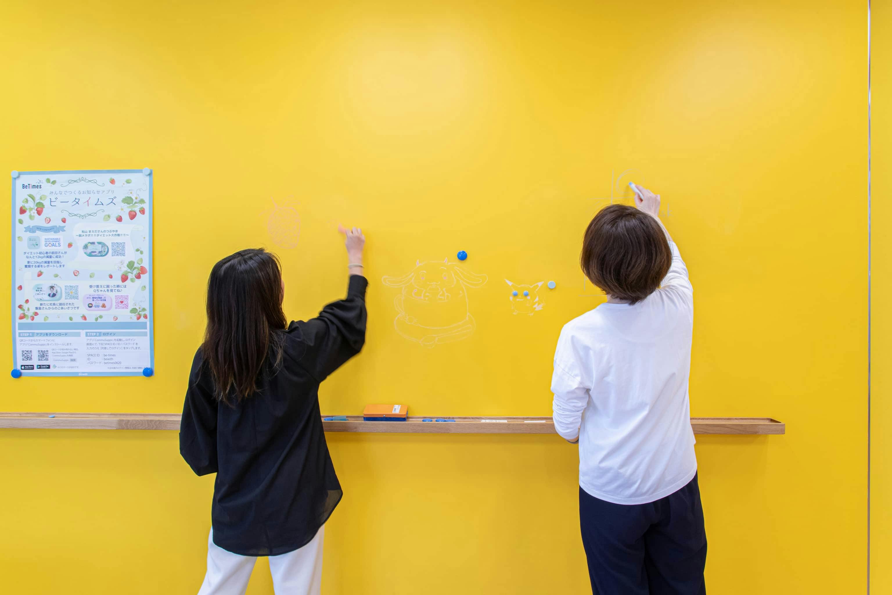 ビーウィズ株式会社 様の事例写真／[共創エリア]壁の一部には黄色の黒板塗料が塗られており、チョークで書いたり消したりできます。ミーティングなどに利用できるほか、掲示板としても使われています。