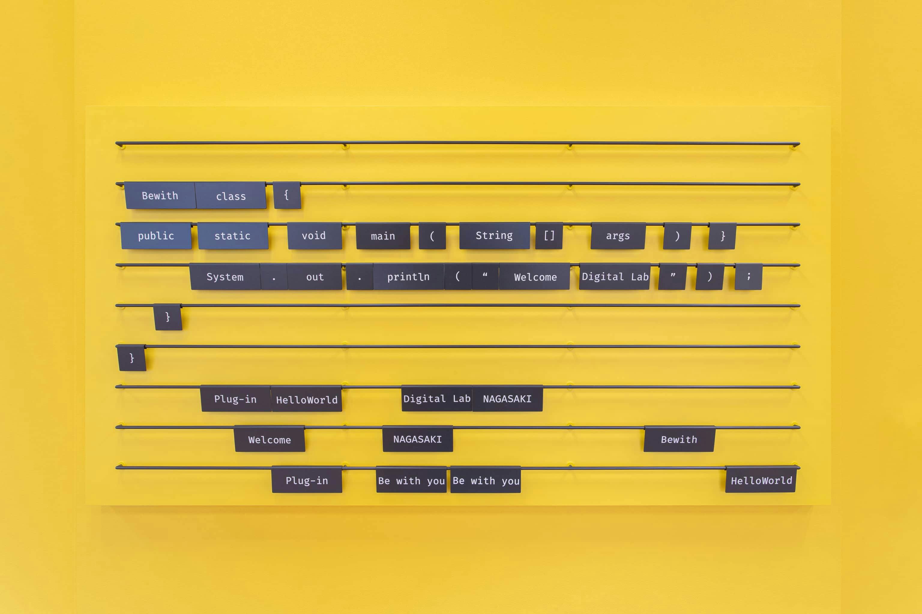 ビーウィズ株式会社 様の事例写真／[コードのプレート]エントランス付近にはメッセージボードを設置。カッティングシートで単語や記号を記した、スチール製のプレートが多数設置されています。プログラミングのコードとして自由に並べ替えることで、来訪者にさまざまなメッセージを伝えられるようになっています。