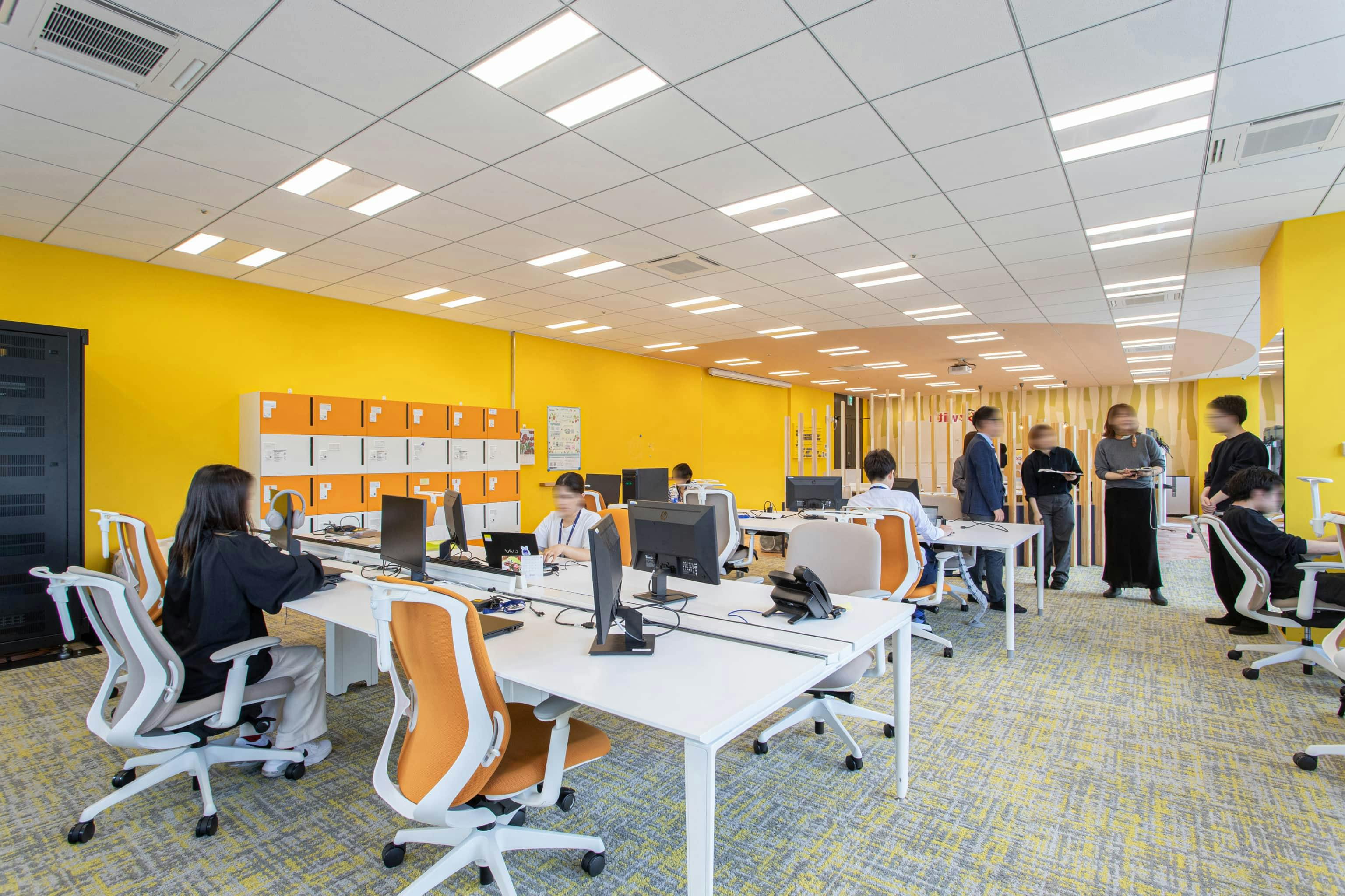 ビーウィズ株式会社 様の事例写真／[執務エリア]床の貼り地や、チェアなどの什器にもビタミンカラーを取り入れ、統一感のあるカラーリングです。私物は壁際に設置したロッカーで個別に管理しています。