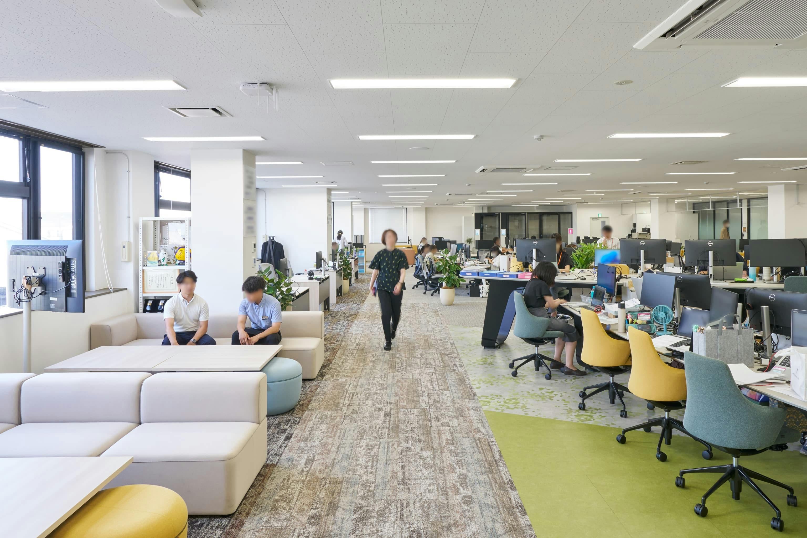 株式会社ウェルパーク 様の事例写真／[執務エリア]やさしいグレートーンにイエローとグリーンが映え、明るい雰囲気です。メイン通路から、すべてのエリアへのアクセスが可能。リラックス感のあるソファラウンジは、気軽な対話や簡単な打ち合わせに使われています。