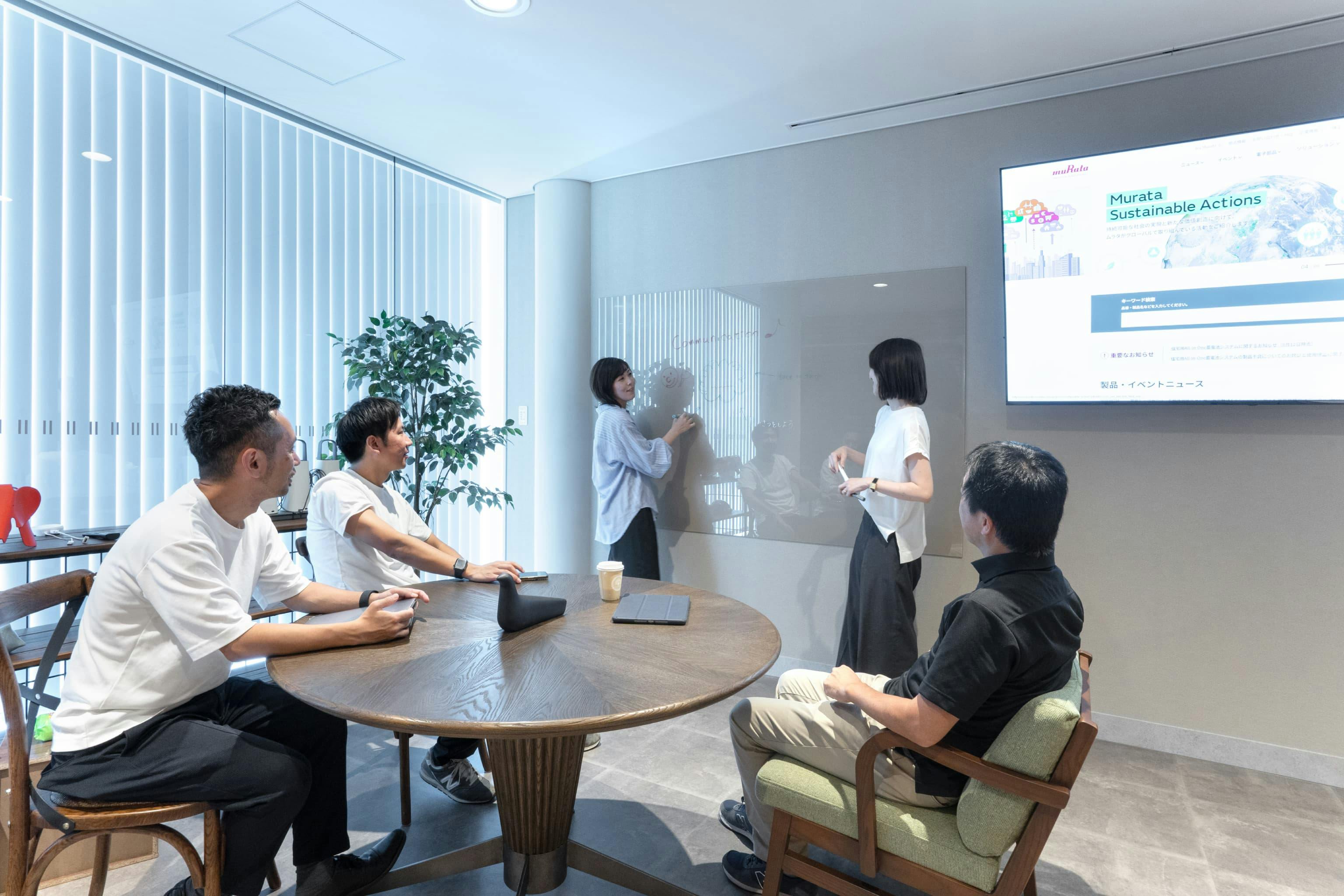 株式会社村田製作所 様の事例写真／[5階食堂会議室]レンガ壁の対面には、大型モニターとクリアボードを設置。背景に溶け込むクリアボードは、ホワイトボードのようにペンで書き込みができます。リラックスした雰囲気の会議やプレゼンテーションにもぴったりです。