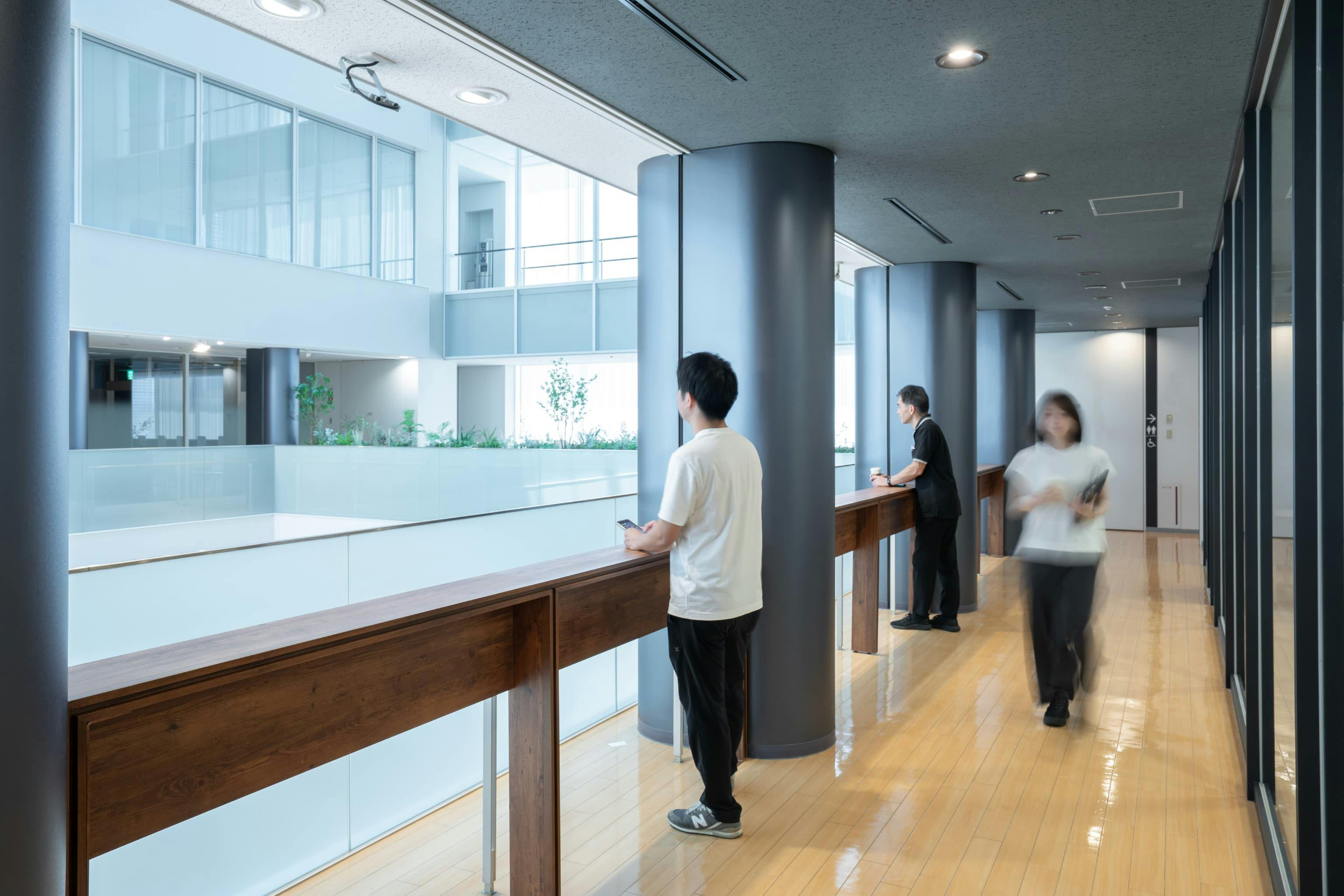 株式会社村田製作所 様の事例写真／[6階リフレッシュエリア]アトリウムに面した通路にある木製カウンター。食堂フロアを見下ろしながら作業したり、ドリンク片手に仲間と談笑したり。階下に緑のある空間が広がっているからこそ、廊下も憩いの場に変わります。