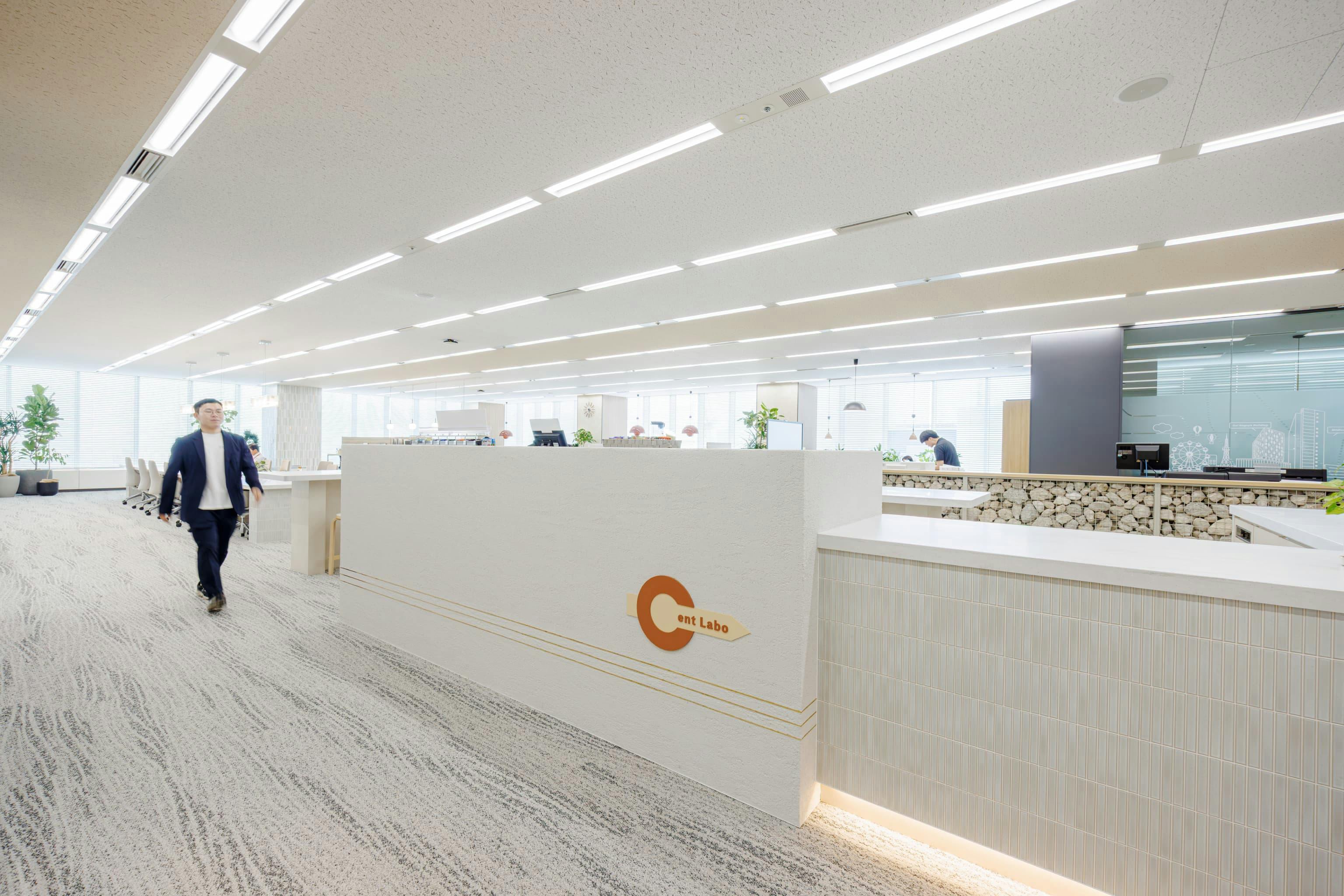 株式会社オカムラ 名古屋ラボオフィス『Cent Labo』の事例写真／[エントランス（ランウェイエリア内）]「ランウェイ」は、エントランスから執務エリアに通じるメイン通路の役割も果たします。エントランス正面に設けたL字カウンターは、カフェスペースやゴミ箱などを背面に隠すための立ち上がりとなっています。