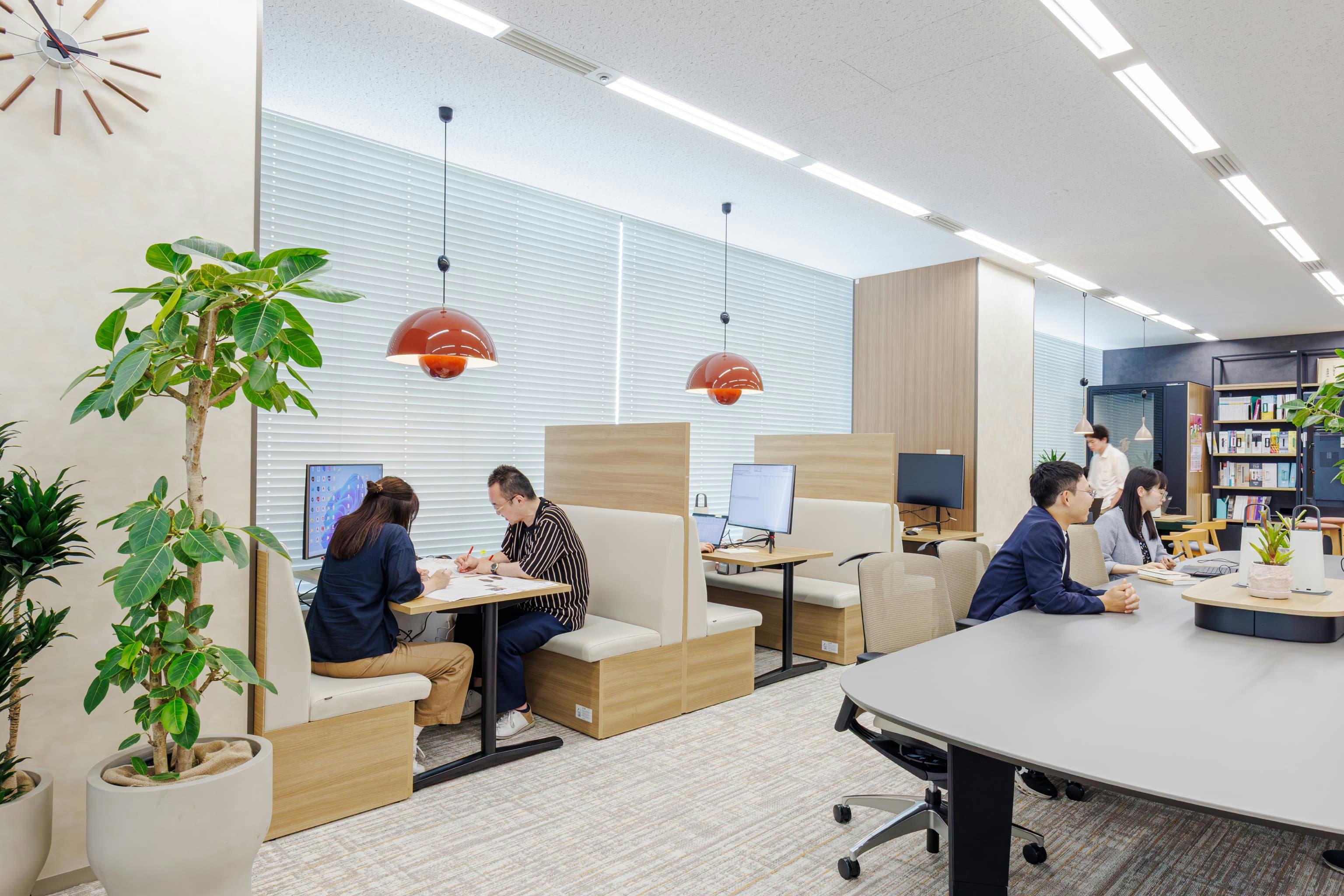 株式会社オカムラ 名古屋ラボオフィス『Cent Labo』の事例写真／[執務エリア]既存の柱を利用し、籠り感を演出したファミレス席は人気のスポット。明るい木目の家具と暖色のポップなペンダントライトが配されたカジュアルな雰囲気で、ミーティングも和やかに進みます。