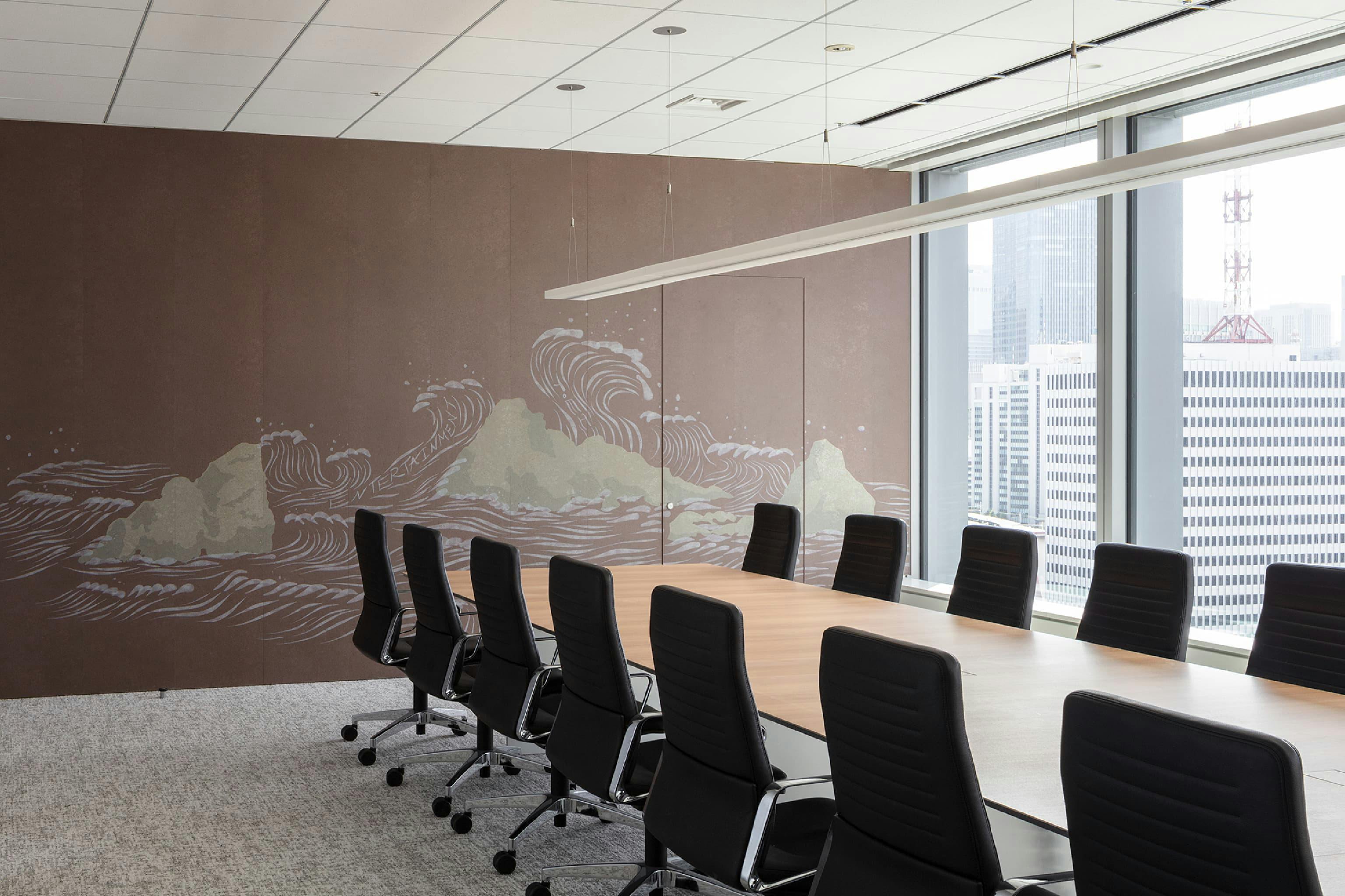 東映株式会社 様の事例写真／[9階 会議室]自然光が差し込む会議室には、壁面に荒波と岩を描いたオリジナルグラフィックが施されています。目を凝らすと「TOEI」「ENTERTAINMENT」の文字が。遊び心にあふれ、会話のきっかけにもなるデザインです。