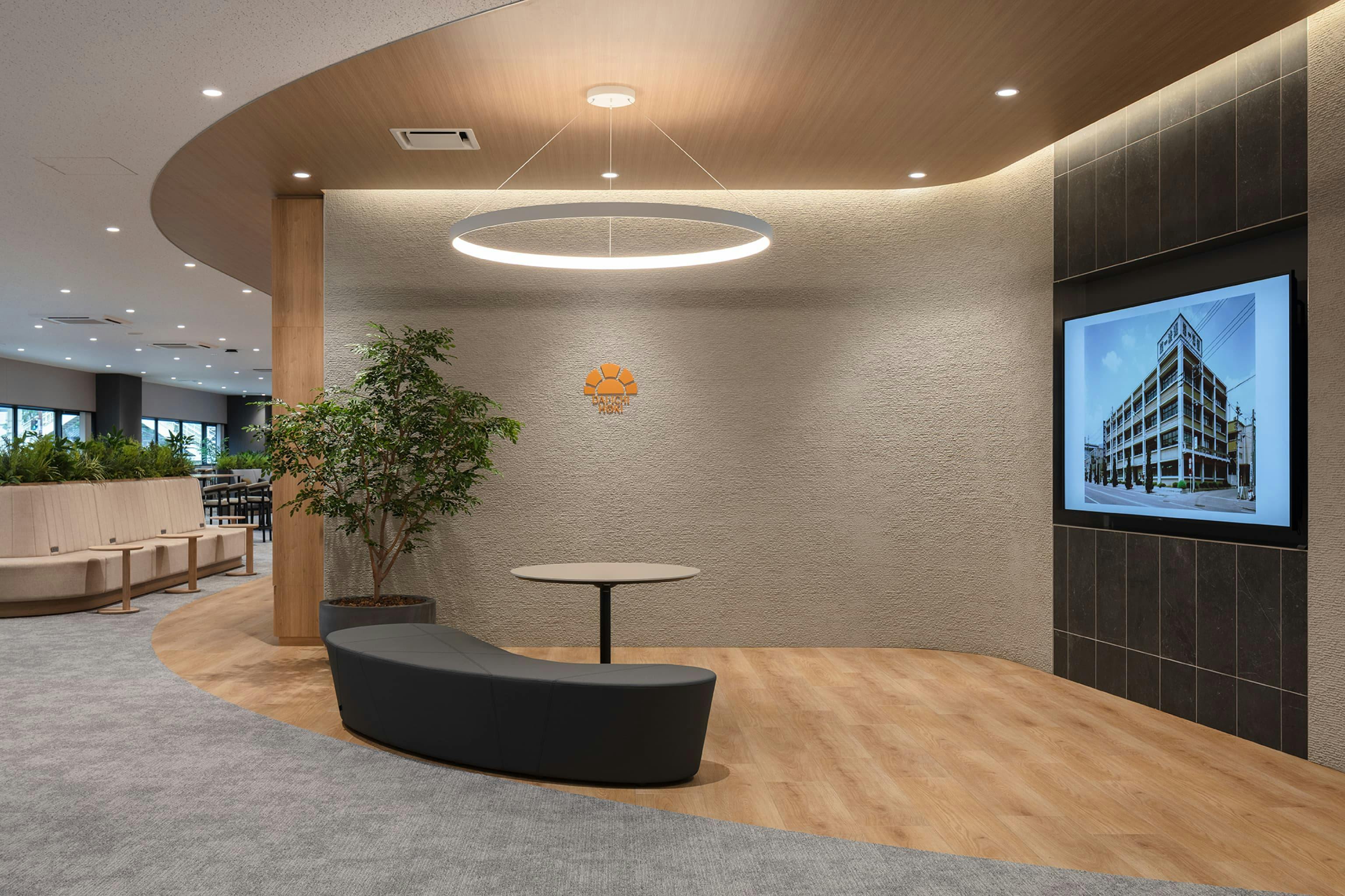 第一法規株式会社 様の事例写真／[1Fエントランス]企業ロゴマークの色調に合わせて暖色でまとめられたエントランス。ラウンド形状の照明やソファは柔軟性のある社風を、直線状のタイルは第一法規の変わらない堅実さを表現しています。