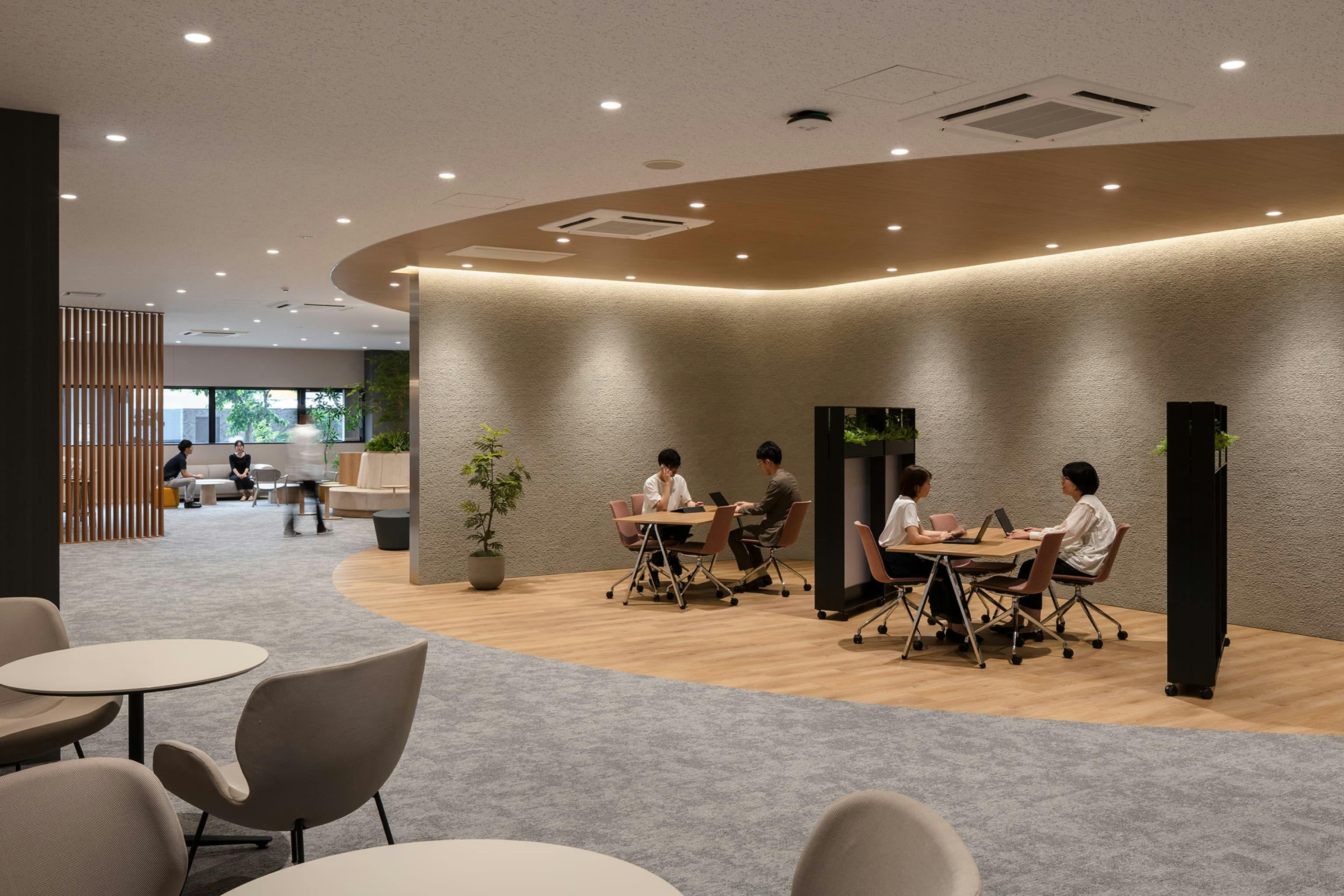 第一法規株式会社 様の事例写真／[1F商談スペース]社外PRスペースの近くには、取引先との商談スペースが用意されており、会社を知ってもらった後に落ち着いて話ができる動線になっています。壁は設けずに、天井と床材を貼り分けてゆるやかにゾーニングされています。