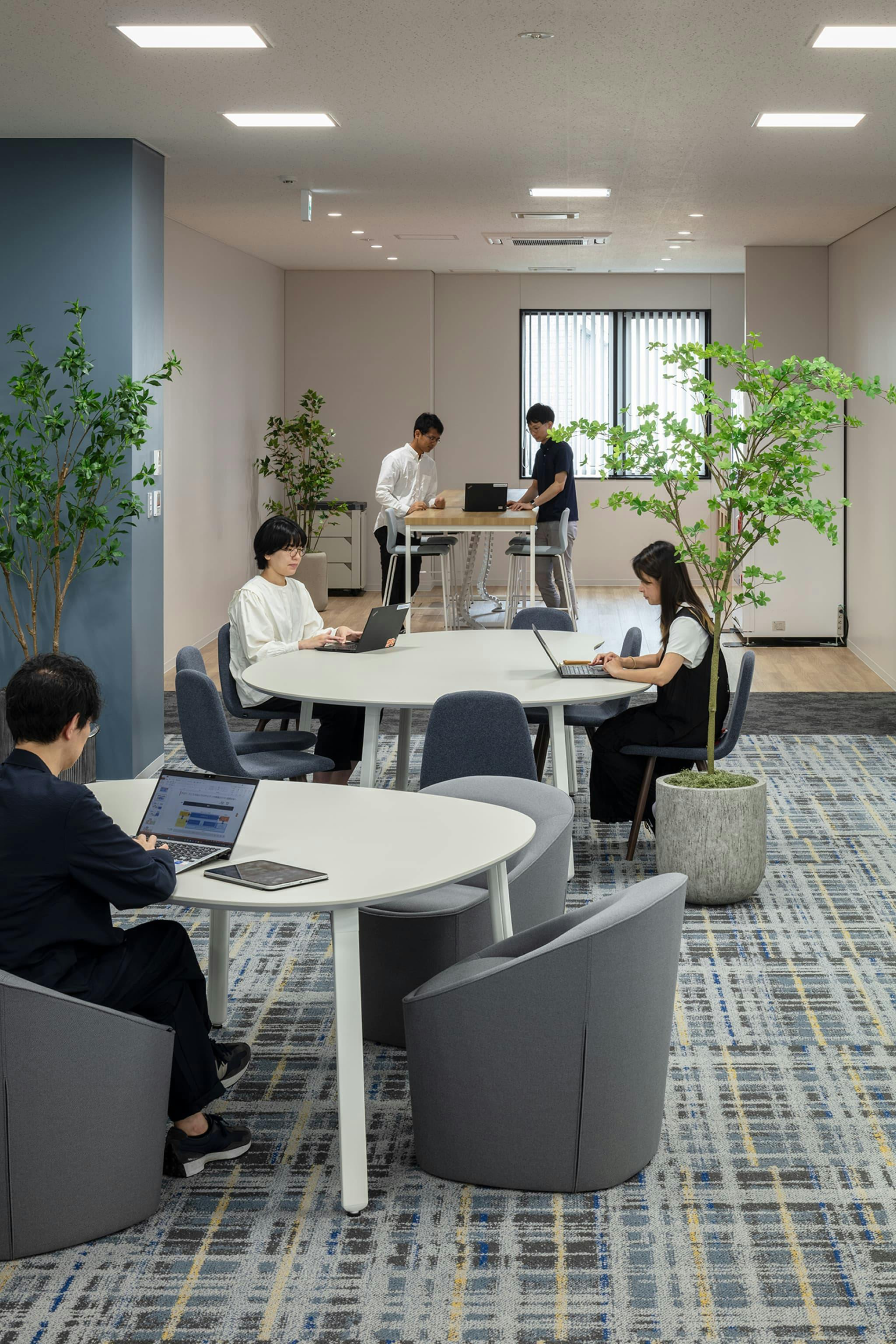 第一法規株式会社 様の事例写真／[3F執務フロア（リフレッシュスペース）]執務フロアの一角に設けられたリフレッシュスペースは、チェック柄のカーペットでカジュアルな雰囲気。一息つきたいときや少人数のカジュアルな打ち合わせに利用されています。原稿をテーブルに広げて編集作業をする人も。