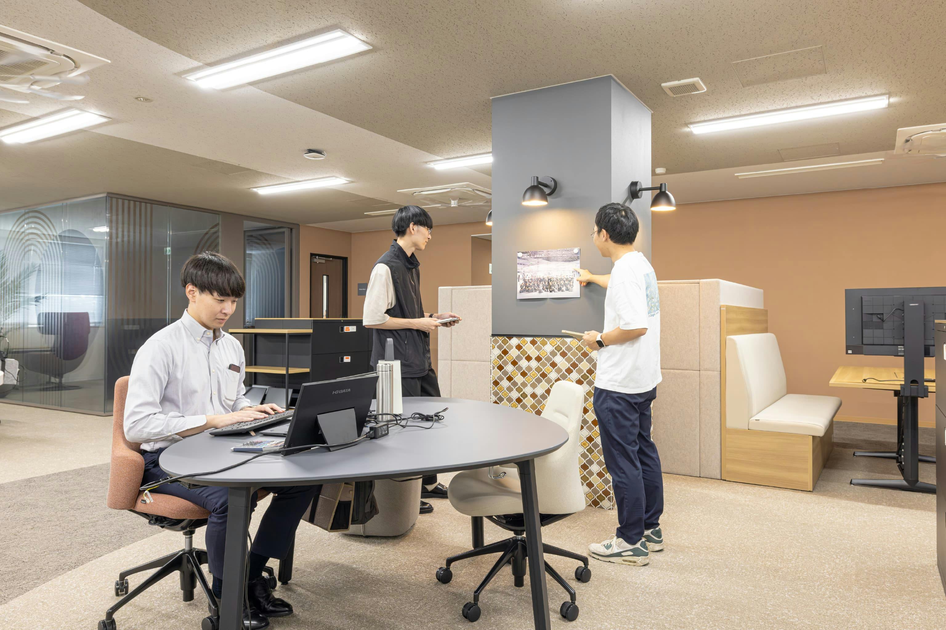 日本ガスケット株式会社 様の事例写真／[コネクトエリア]設計上、取り除けなかった鉄骨の柱は、上部に黒板仕様のシートを貼って掲示板として活用。下部は地元の東海地方で製造されたタイルで装飾しています。意匠性が高く、人が集まるスペースとして生かされています。