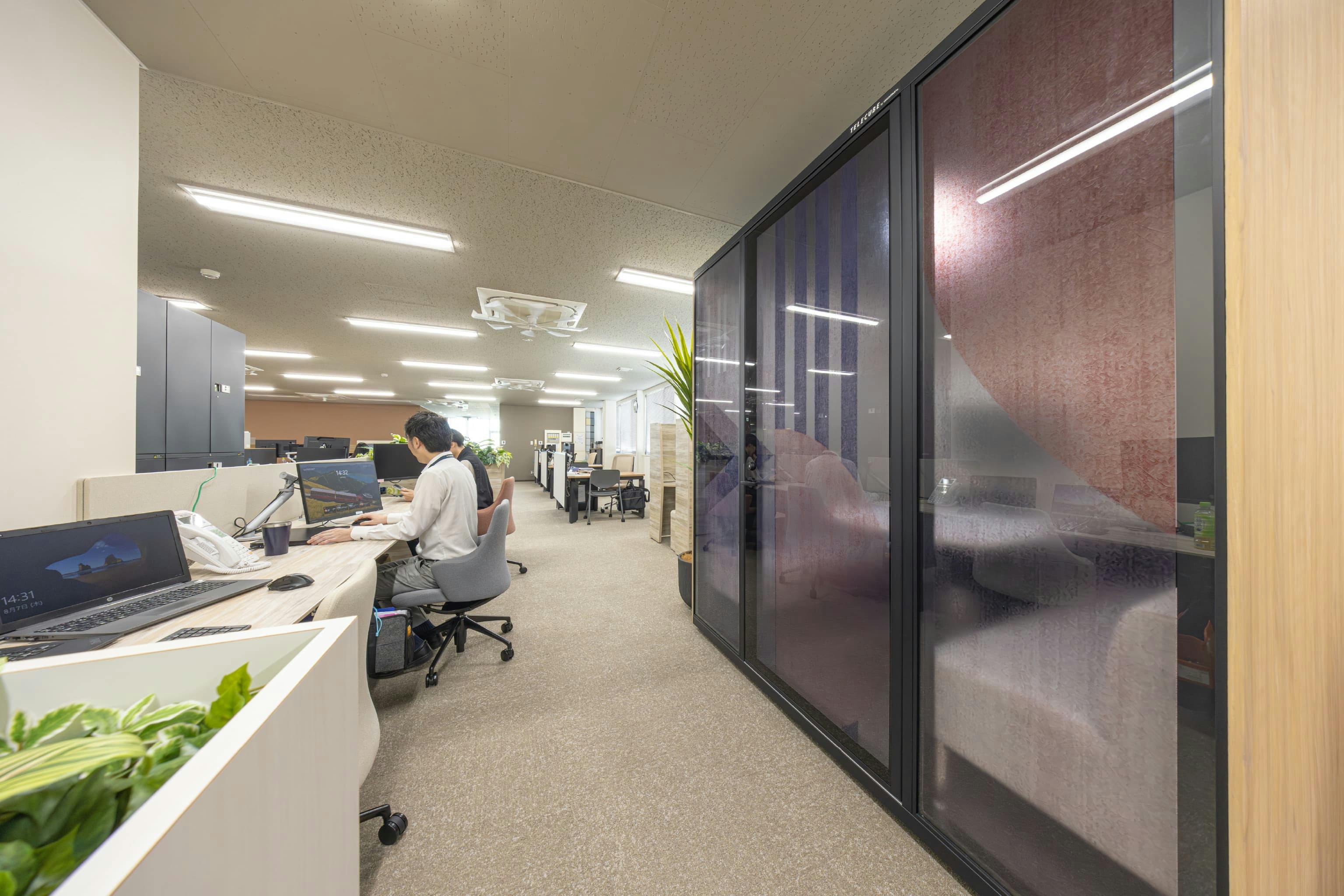 日本ガスケット株式会社 様の事例写真／[フルクローズ型ワークブース（執務エリア）]少人数の会議は、執務エリア内の4人用フルクローズ型ワークブースで行われることも。向かいに経理チームのデスクが並んでいるため、個人情報の写った画面が見えないようにガラス窓に目隠し効果のあるデザインシートが貼られています。