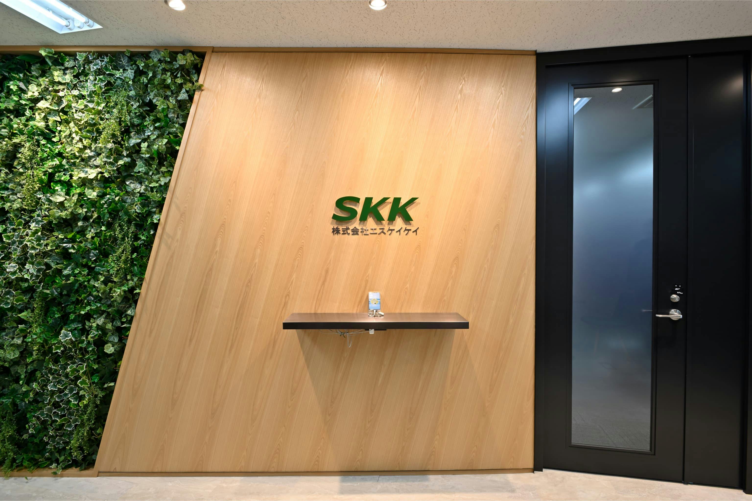 株式会社エスケイケイ 様の事例写真／[エントランス]植栽を施した壁面と本物の木材を用いたパネルという有機的な素材を組み合わせることで、空間がナチュラルな印象に。システム開発会社が抱かれがちな無機質なイメージをやわらげ、親しみやすい雰囲気が生まれています。