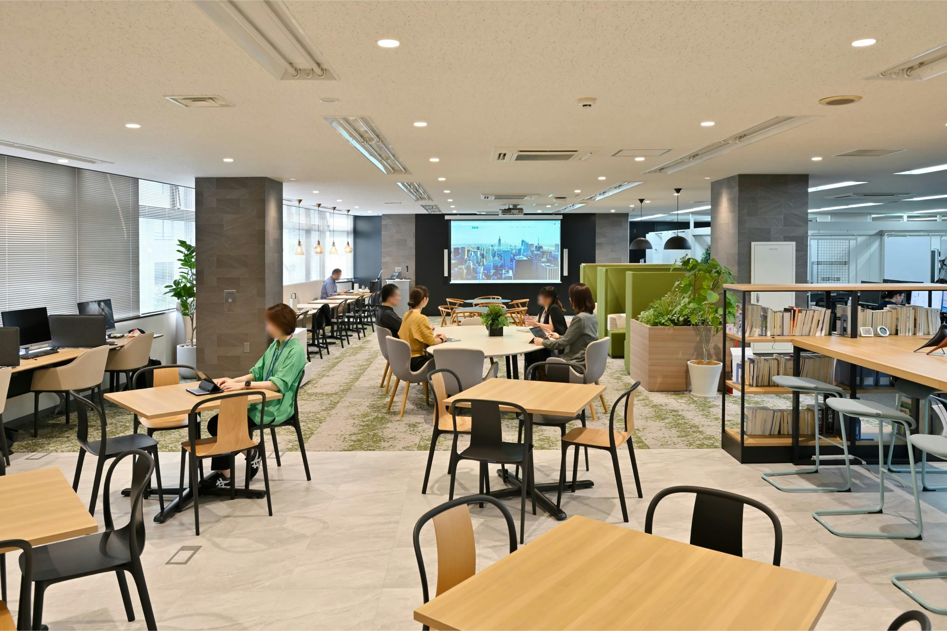 株式会社エスケイケイ 様の事例写真／[交流エリア（カフェスペース）]動かしやすい什器が配置され、レイアウトは自由自在。テーブルを寄せてグループで食事したり、椅子を端に動かして立食の懇親会を開いたりと、多目的に活用できます。社員同士の交流やリフレッシュの時間が広がる場です。