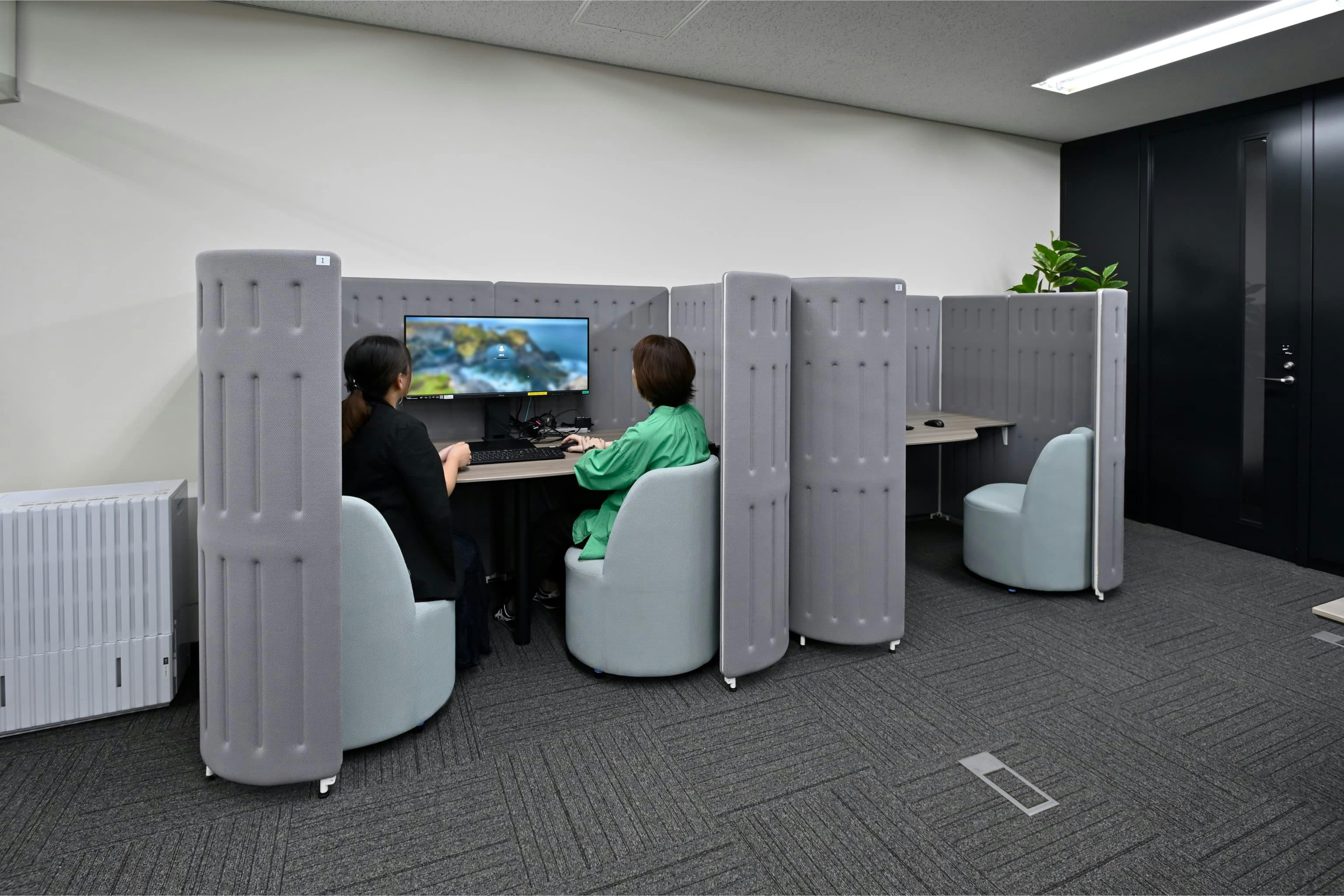 株式会社エスケイケイ 様の事例写真／[執務エリア]ペアワークブースは、2人で同じモニターを見ながら作業できる席です。業務の確認や新人教育のほか、面談にも活用されています。椅子を横並びで配置しているため、対面より緊張しにくく、話しやすいと評判です。