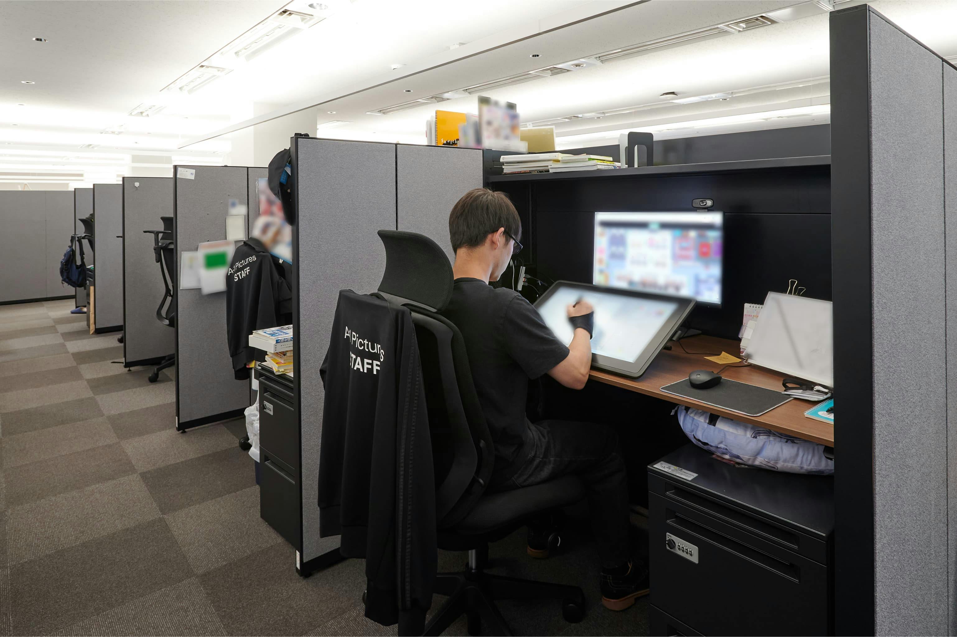 株式会社A-1 Pictures 様の事例写真／[S棟3F・作画フロア]幅1600mmのワイドな電動昇降デスクに、上部棚を備えた作業席。チェアは体格に合わせて自然にフィットし、ヘッドレストとハンガー付きで快適。自分らしい空間に整えられ、心地よい姿勢で制作に専念できます。