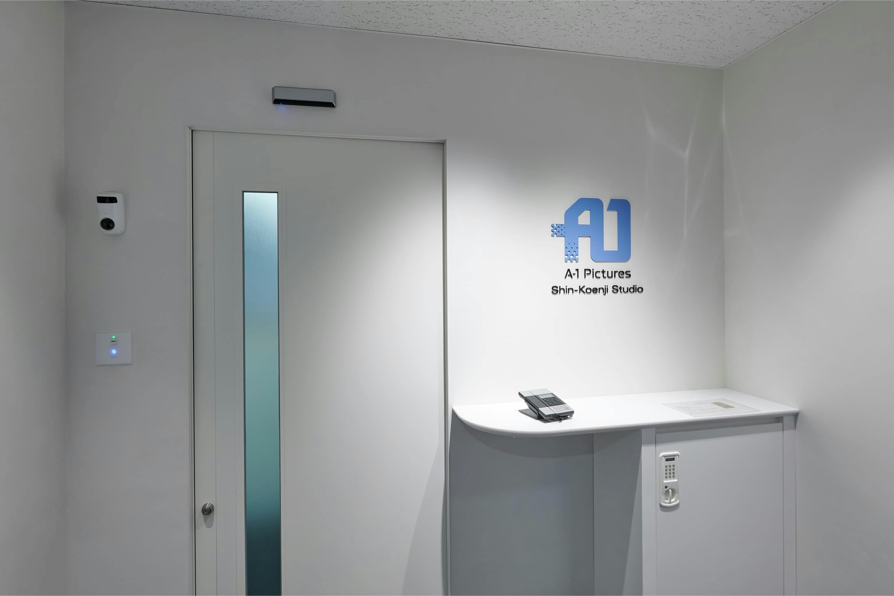 株式会社A-1 Pictures 様の事例写真／[N棟3Fエントランス]必要な機能をコンパクトにまとめ、照らし出された企業ロゴと緩やかな曲線のカウンターが、シンプルな空間のアクセントに。入口を最小限に抑えた構成により、その先に続く執務エリアにゆとりをもたらしています。