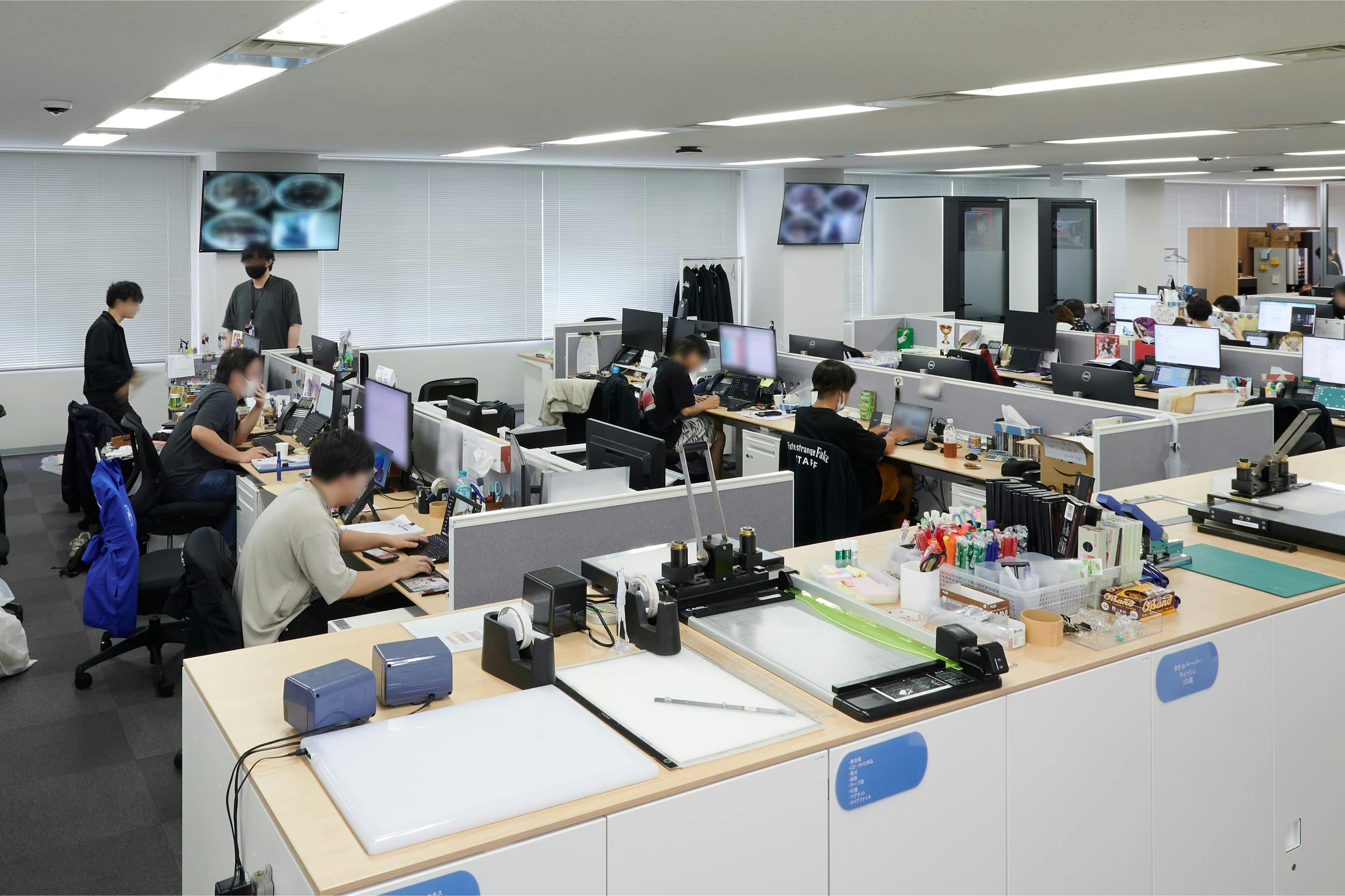 株式会社A-1 Pictures 様の事例写真／[N棟3F執務エリア]通路沿いのキャビネットは天板付きで、作業台としても活用されています。作画用紙を扱う様子は、アニメ制作会社ならではの光景です。現場のニーズを的確に捉えた設計の工夫が随所に感じられます。