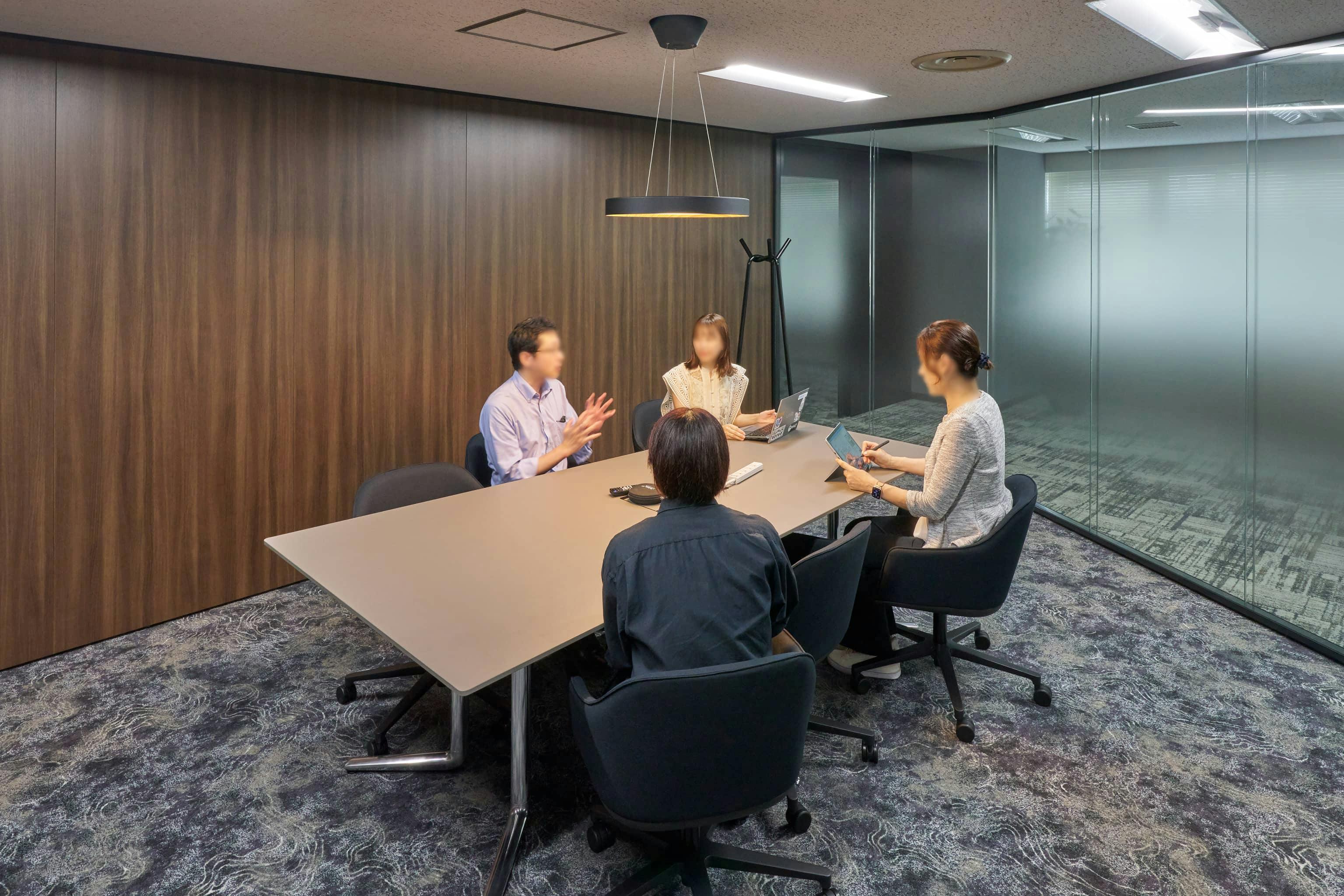 ジェイエスフィット株式会社 様の事例写真／[5F応接室]素材感のある内装とモダンな什器が調和し、上質な雰囲気。来客対応や商談の場にふさわしい、安心感と品格を兼ね備えています。自然光を取り込むガラスの仕切りが閉塞感を和らげ、緊張感をほぐす効果も。親密な対話が生まれます。