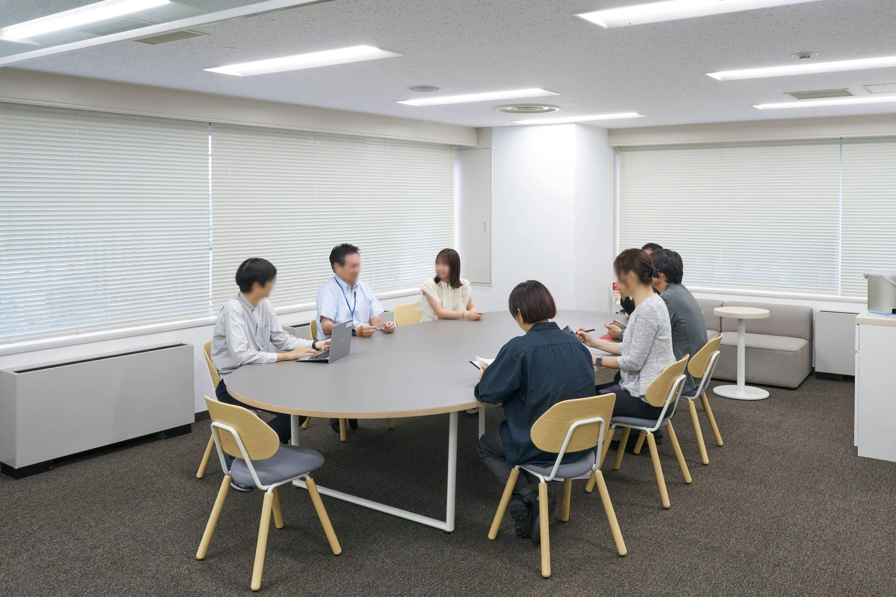 ジェイエスフィット株式会社 様の事例写真／[7F ABWエリア]オーバルテーブルは大人数のミーティングに対応。出社する人が多い日は個人の執務席としても利用できます。リモートワークとのハイブリッドスタイルのなかで、柔軟に活用されています。