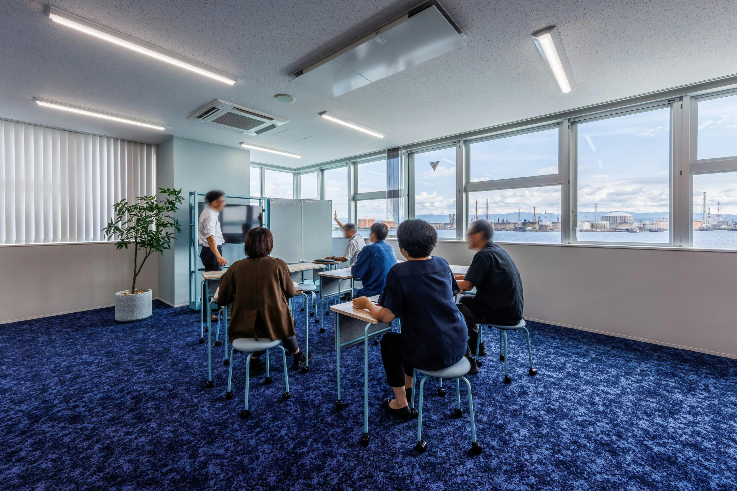 エア・ウォーター・エンジニアリング株式会社 様の事例写真／[3F ABWエリア]軽くて自在に動かせるデスクとチェアは、人数もレイアウトも選びません。モニターと合わせてスクール形式で並べれば、社内勉強会やプレゼンの場に早変わり。大阪湾の景色を横目に、のびのびとした雰囲気が漂います。