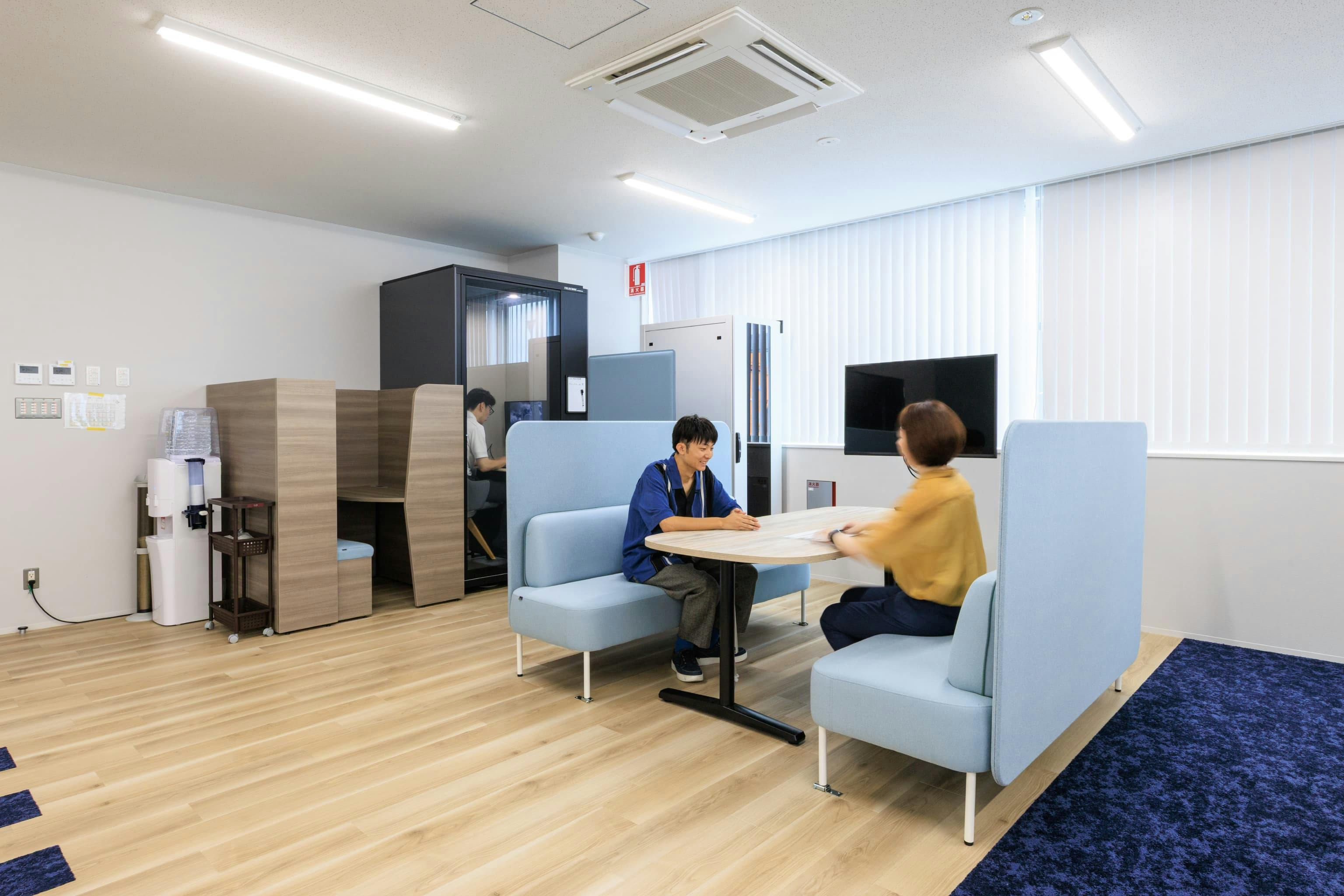 エア・ウォーター・エンジニアリング株式会社 様の事例写真／[5F ABWエリア]対面での和やかな打ち合わせにはファミレス席が人気です。通路沿いのオープンエリアにありながら、ソファの背もたれに取り付けた吸音パネルが周囲のざわめきや視線をほどよく遮り、落ち着き感をもたらしています。