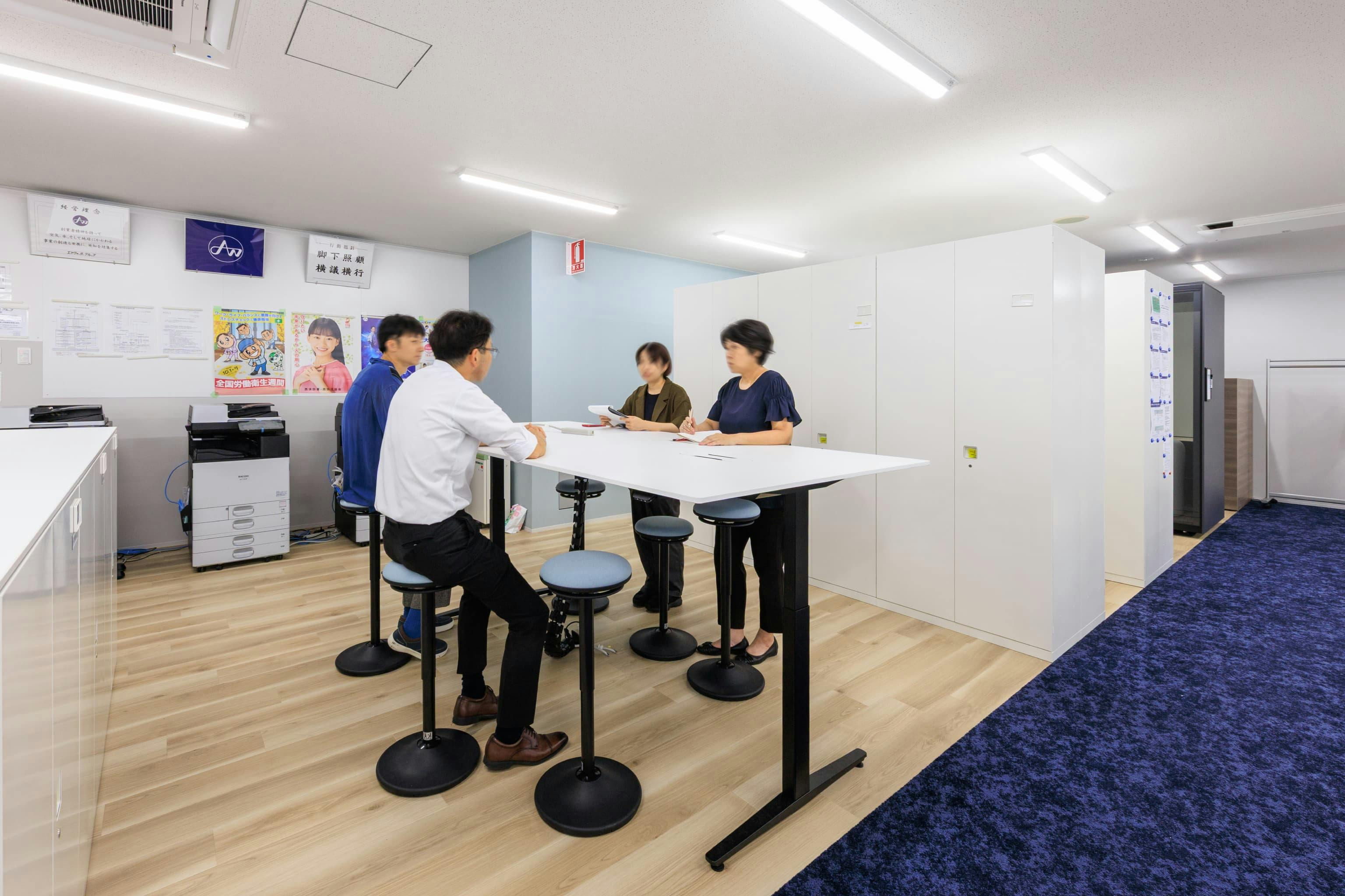 エア・ウォーター・エンジニアリング株式会社 様の事例写真／[3F ABWエリア]大型の電動昇降デスクは立ち作業にも便利。プリンターから出力した図面を囲んでそのまま話し合いに取りかかることができ、通りがかった人が会話に参加することも。