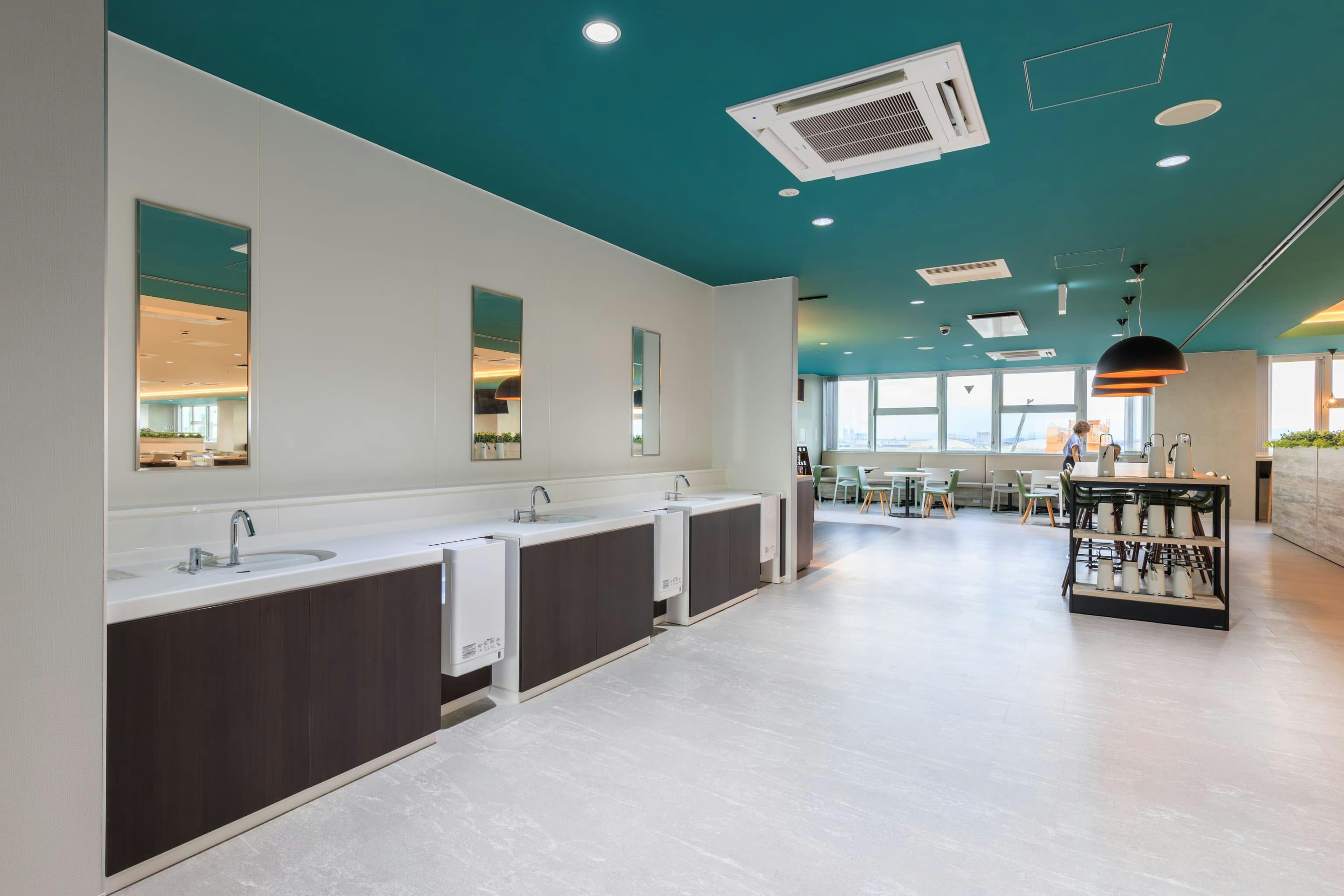エア・ウォーター・エンジニアリング株式会社 様の事例写真／[6F食堂]食堂の入り口は通路幅を広く設け、混雑時の出入りをスムーズに。自動水栓の流し台を設置し、感染症対策を促します。水が飛びやすい壁面には、グループ会社が扱う抗菌効果に優れたウォール素材が用いられています。