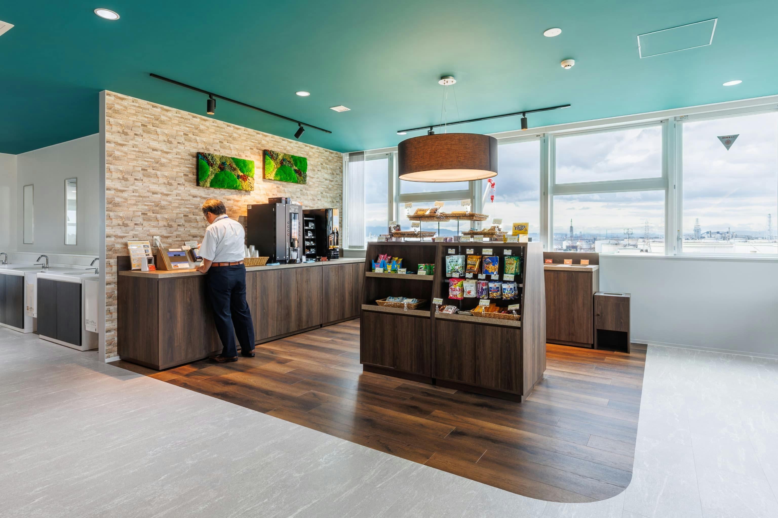 エア・ウォーター・エンジニアリング株式会社 様の事例写真／[6Fカフェコーナー]気軽に利用できるよう、入り口付近に設けられたカフェコーナー。落ち着いたブラウンの什器でまとめられ、くつろいだ気分を引き立てます。軽食やドリンクが購入でき、社員の気分転換の場になっています。