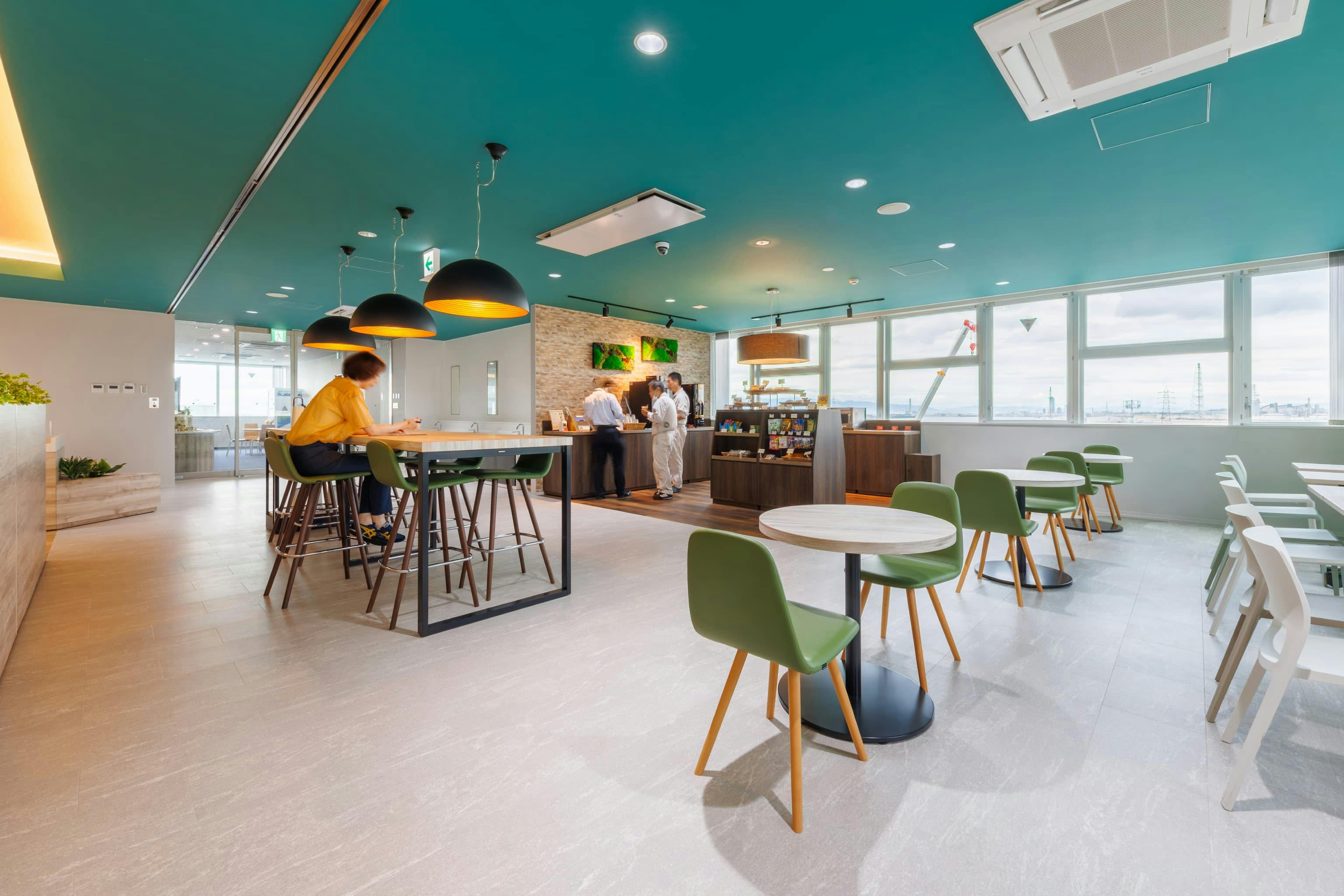 エア・ウォーター・エンジニアリング株式会社 様の事例写真／[6Fカフェコーナー]カフェコーナーで軽食を購入して、近くのハイテーブルやテーブル席でひと休み。さっと利用するのに便利なだけでなく、ふとした拍子に通りがかった人と雑談が始まることも。