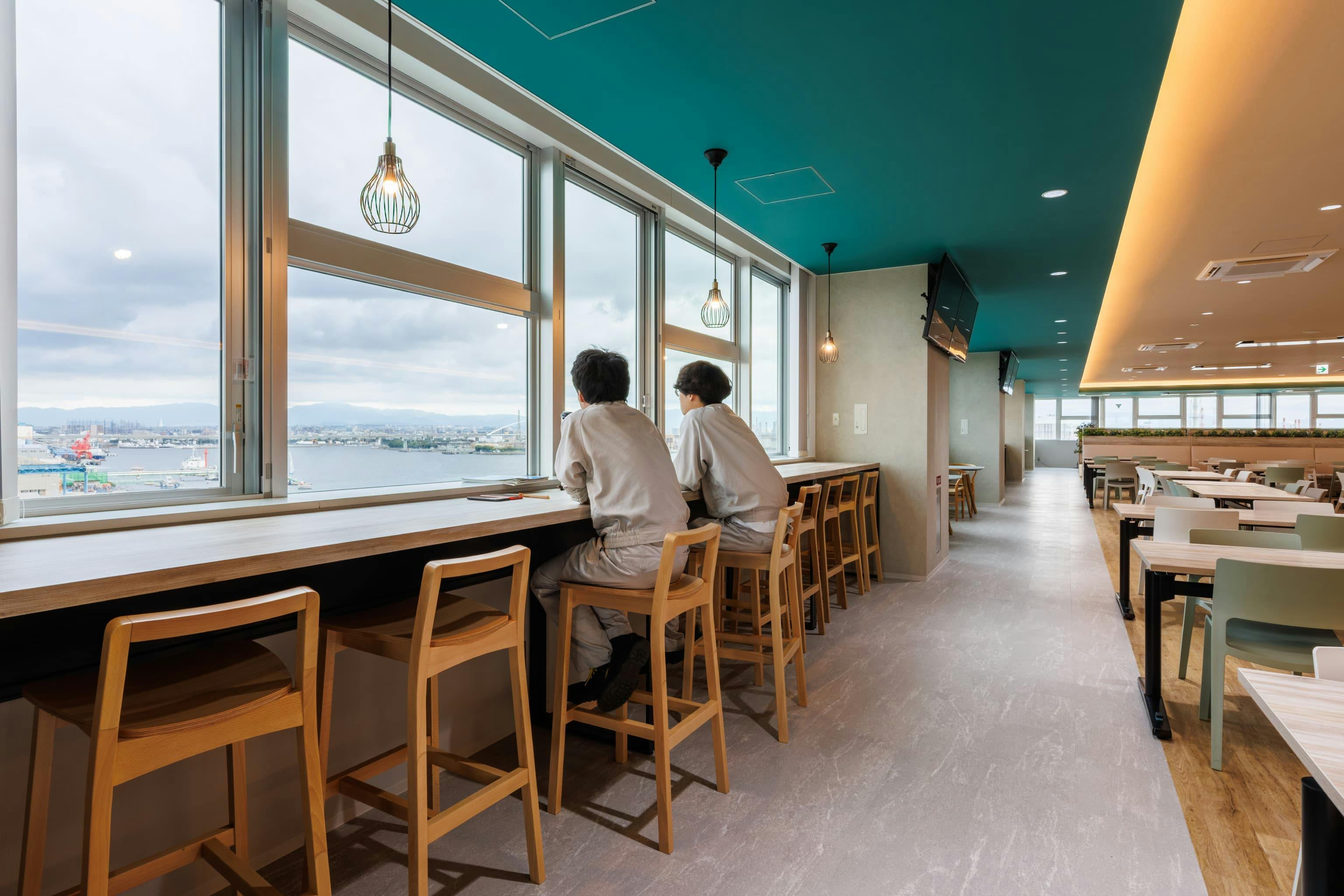 エア・ウォーター・エンジニアリング株式会社 様の事例写真／[6F食堂]窓に向かって設けられたカウンター席では、大阪湾を眺めつつ仕事仲間とコーヒーブレイク。暖色のペンダントライトがともされており、パソコンを持参すればカフェ気分で作業が進みます。
