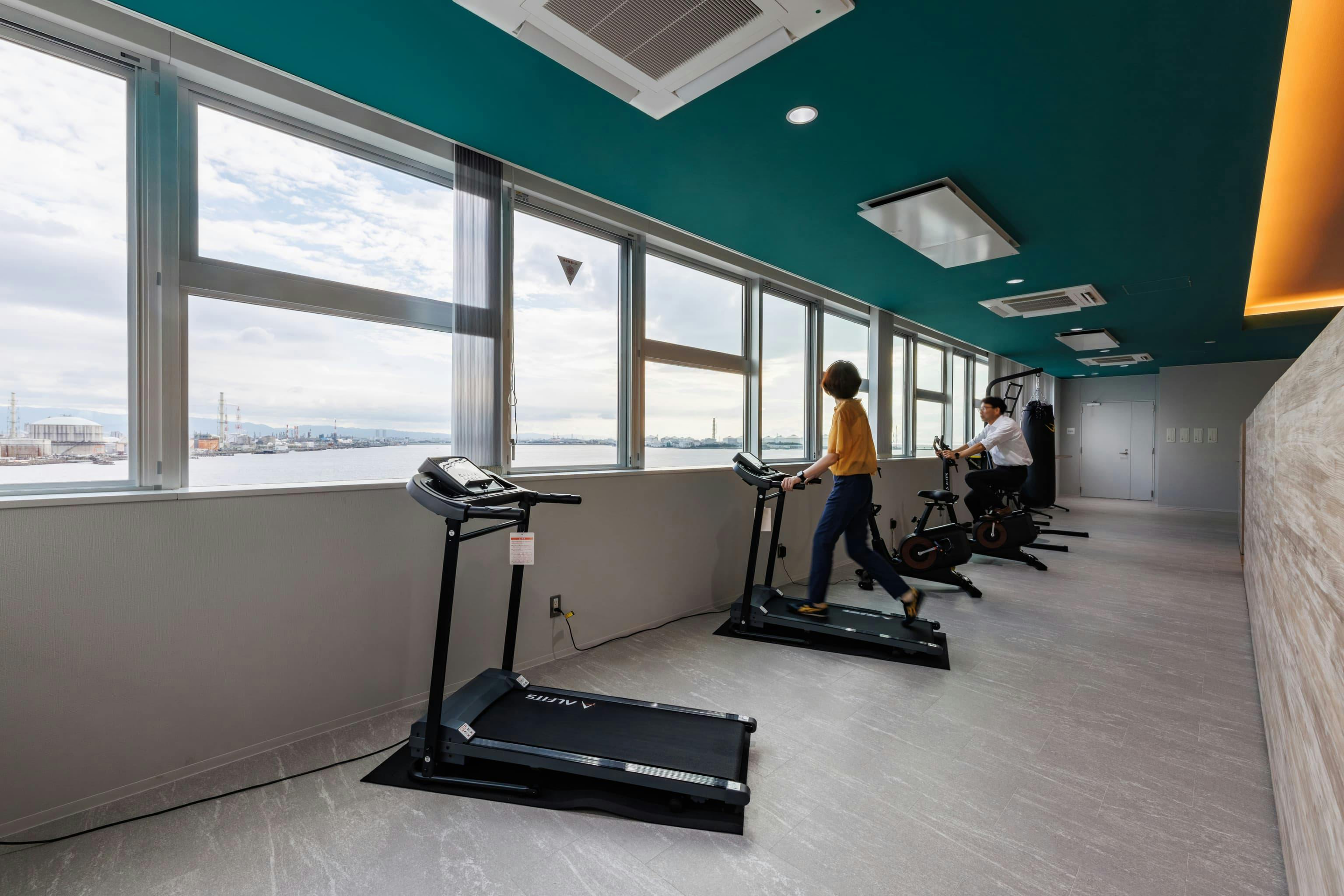 エア・ウォーター・エンジニアリング株式会社 様の事例写真／[6Fエクササイズエリア]仕事で疲れた脳を休めたいときや、体を動かしたいときに、ウォーキングマシンなどのジム機器を利用できます。窓の外には生駒山系の山並みと大きな河口が広がり、遠くを眺めて目を休めるのにもぴったりです。