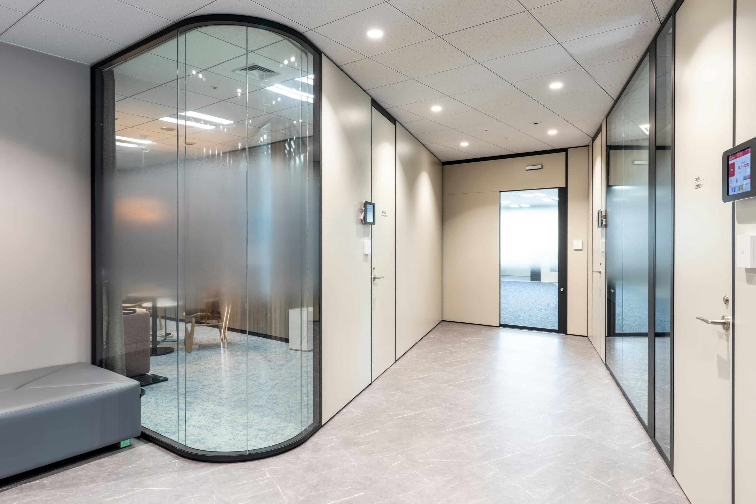 株式会社NTTデータSMS 様の事例写真／[エントランス（健康相談室）]常駐する保健師と面談ができる健康相談室は、執務空間に立ち寄らずに入室できる設計。相談者は同僚と顔を合わせることなく安心して利用できます。曲線ガラスで柔らかさを演出しつつ、相談時はカーテンでプライバシーが確保されます。