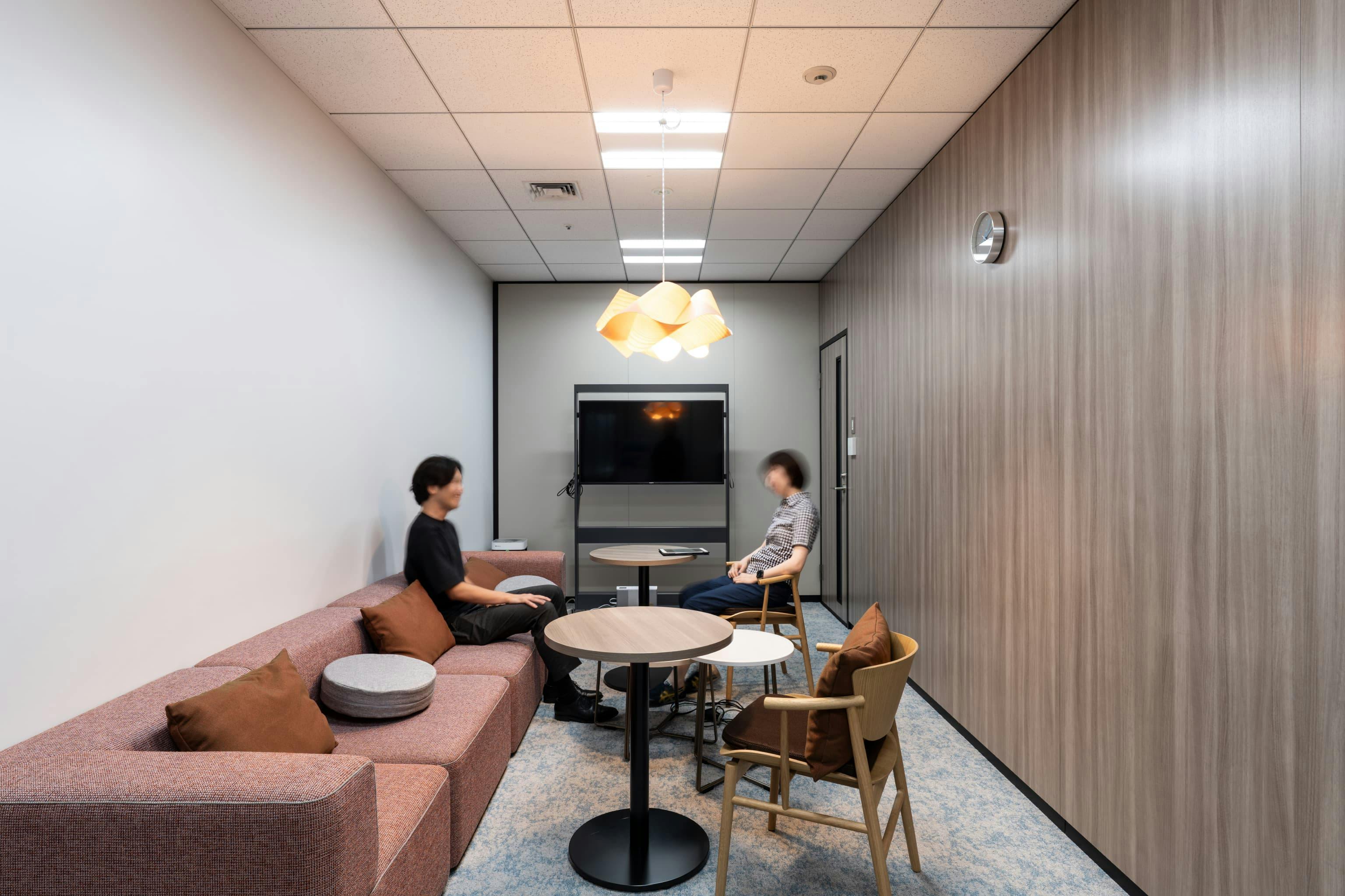 株式会社NTTデータSMS 様の事例写真／[健康相談室]健康経営の一環として設置された健康相談室には、体調の悪い社員が休むための救護室の役割も。木目の壁が印象的な空間に、暖色のファブリックと柔らかな光のペンダントライトが加わり、温もりが漂います。