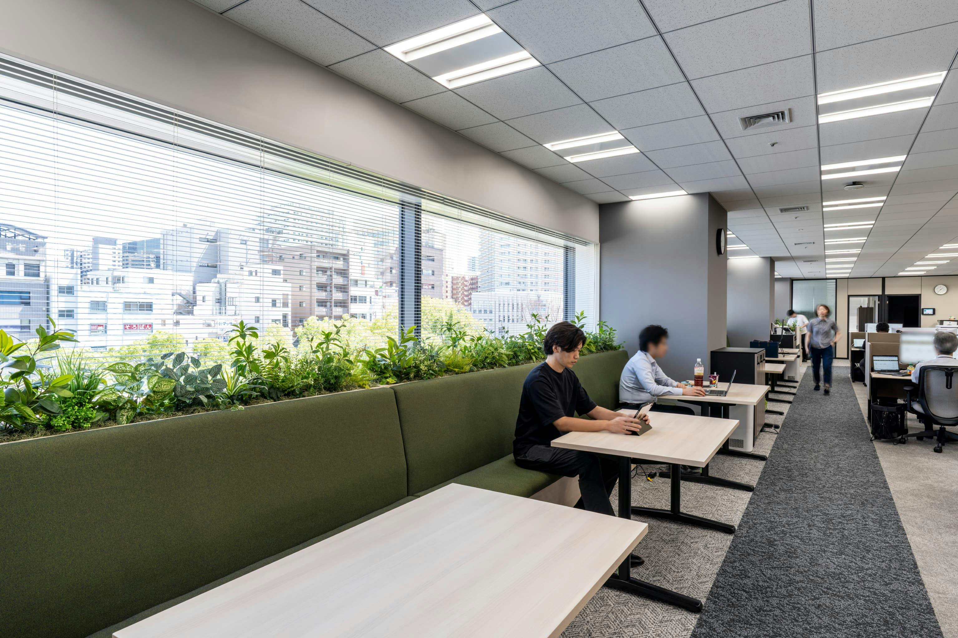 株式会社NTTデータSMS 様の事例写真／[執務エリア]窓際の席は組織長が利用していますが、不在時は一般社員や打ち合わせ用に開放されています。隣に座ってカジュアルに会話を始められるため、会議室を予約しなくても話し合いがしやすくなりました。