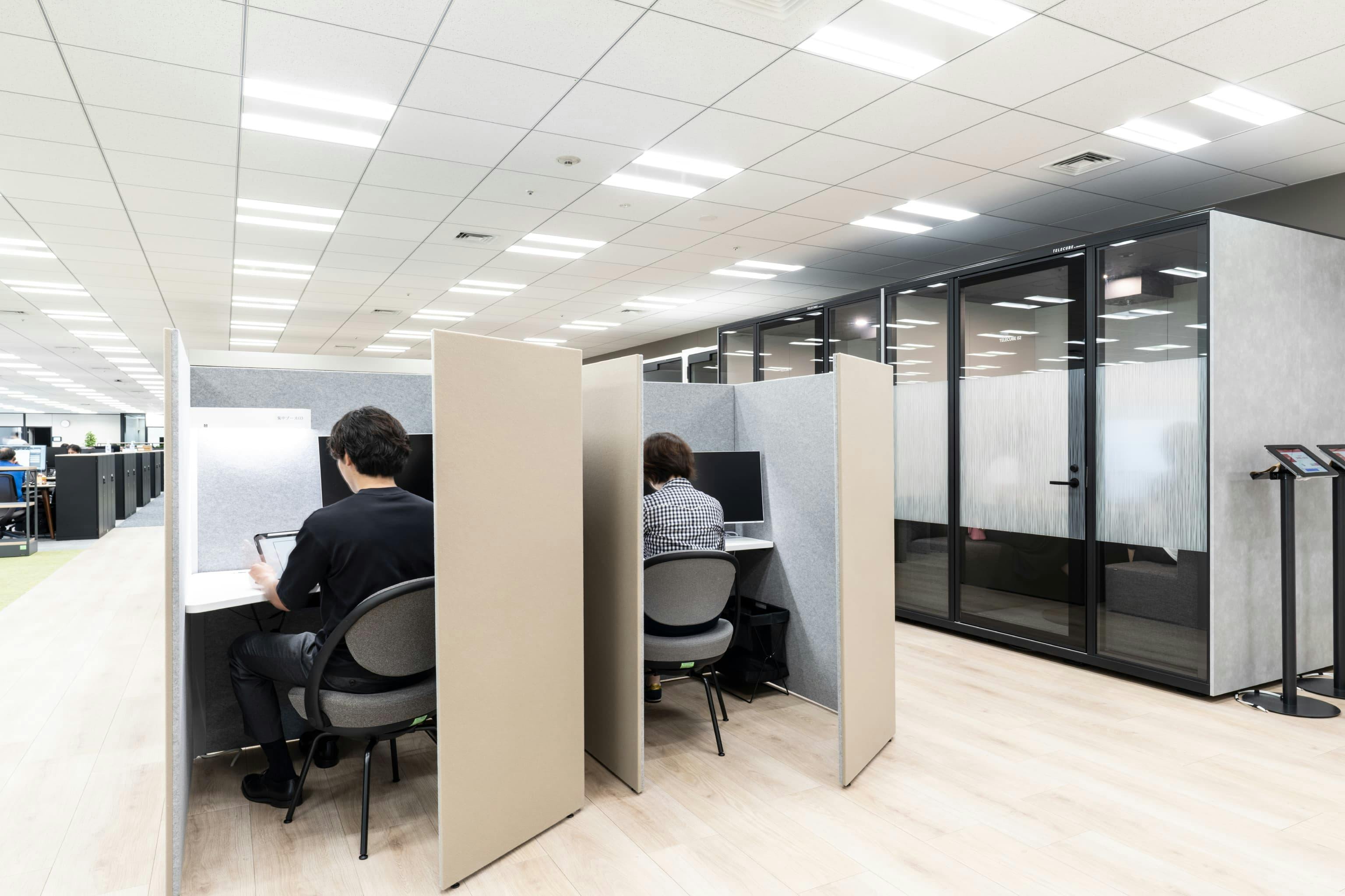 株式会社NTTデータSMS 様の事例写真／[共用エリア“PLAZA”]厚みのあるフェルト仕切りが吸音効果を発揮する集中ブース。デュアルモニターにも対応するサイズのデスクで、作業効率を高めます。隣接するフルクローズ型ワークブースはWeb会議や少人数での打ち合わせに利用されています。