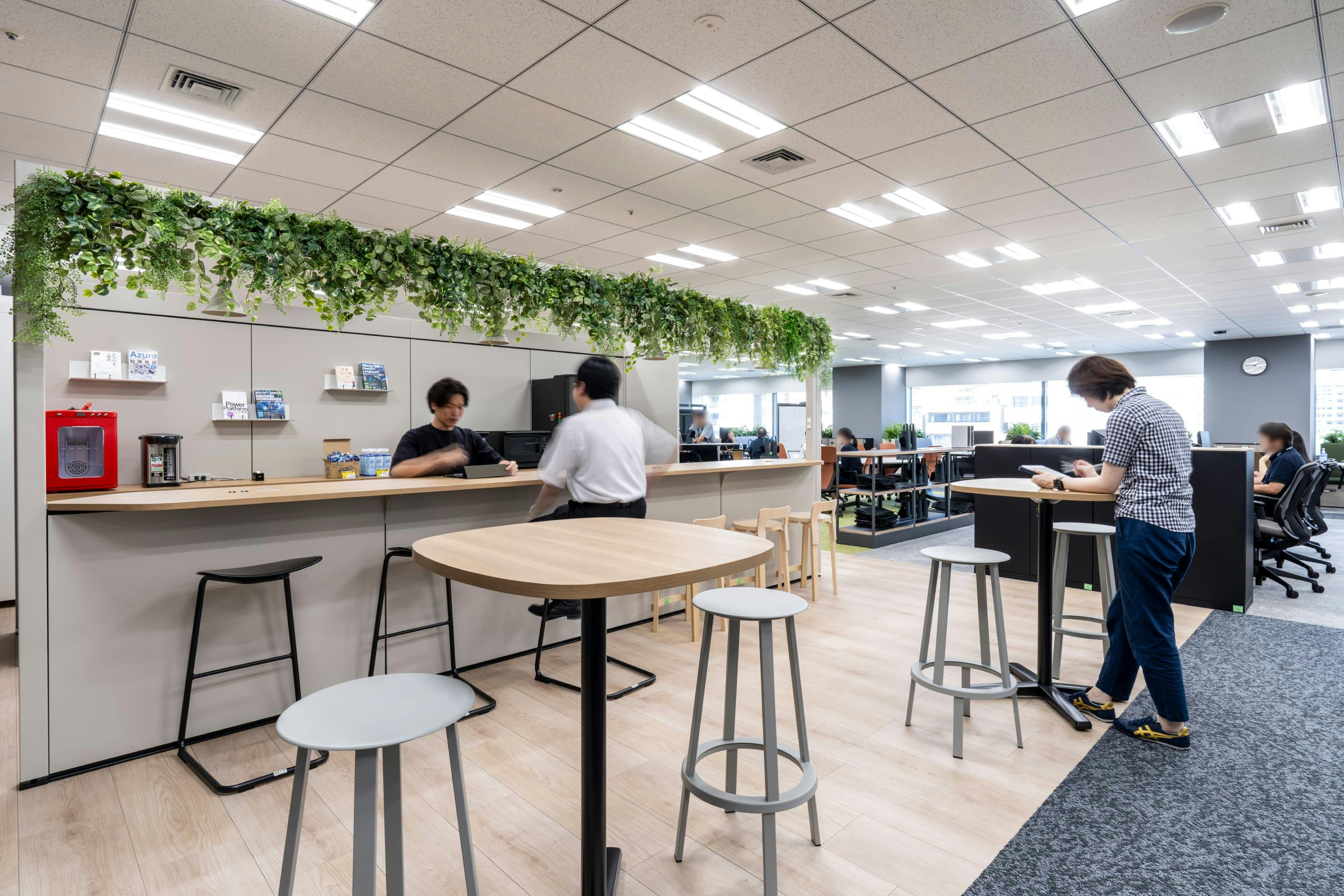 株式会社NTTデータSMS 様の事例写真／[共用エリア“PLAZA”]社員用の入り口付近に設けられたカフェスペース。社員が行き交う位置にあるため、顔を合わせやすく、挨拶をきっかけに話が弾みます。昼食や休憩の場としても活用され、ここから気持ちを切り替えて業務に向かえます。