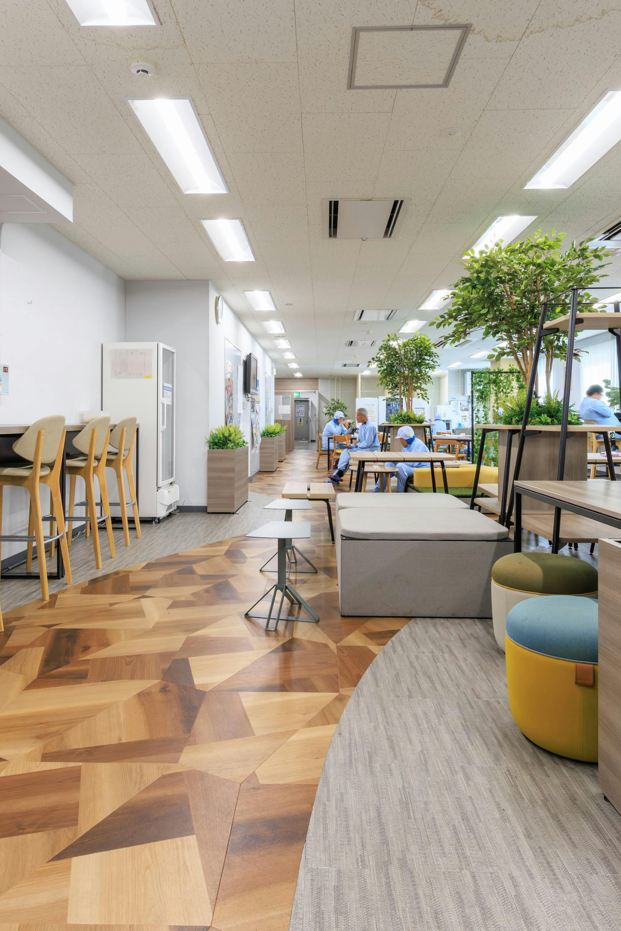 TOPPAN株式会社 ／ TOPPANパッケージプロダクツ株式会社 様の事例写真／[休憩エリア 通路]木の小道をイメージして貼り分けられた床は、公園らしさを演出するとともに、動線を明確にする役割も。ゆるやかなカーブを描くデザインが、ポップで楽しげな印象をもたらします。