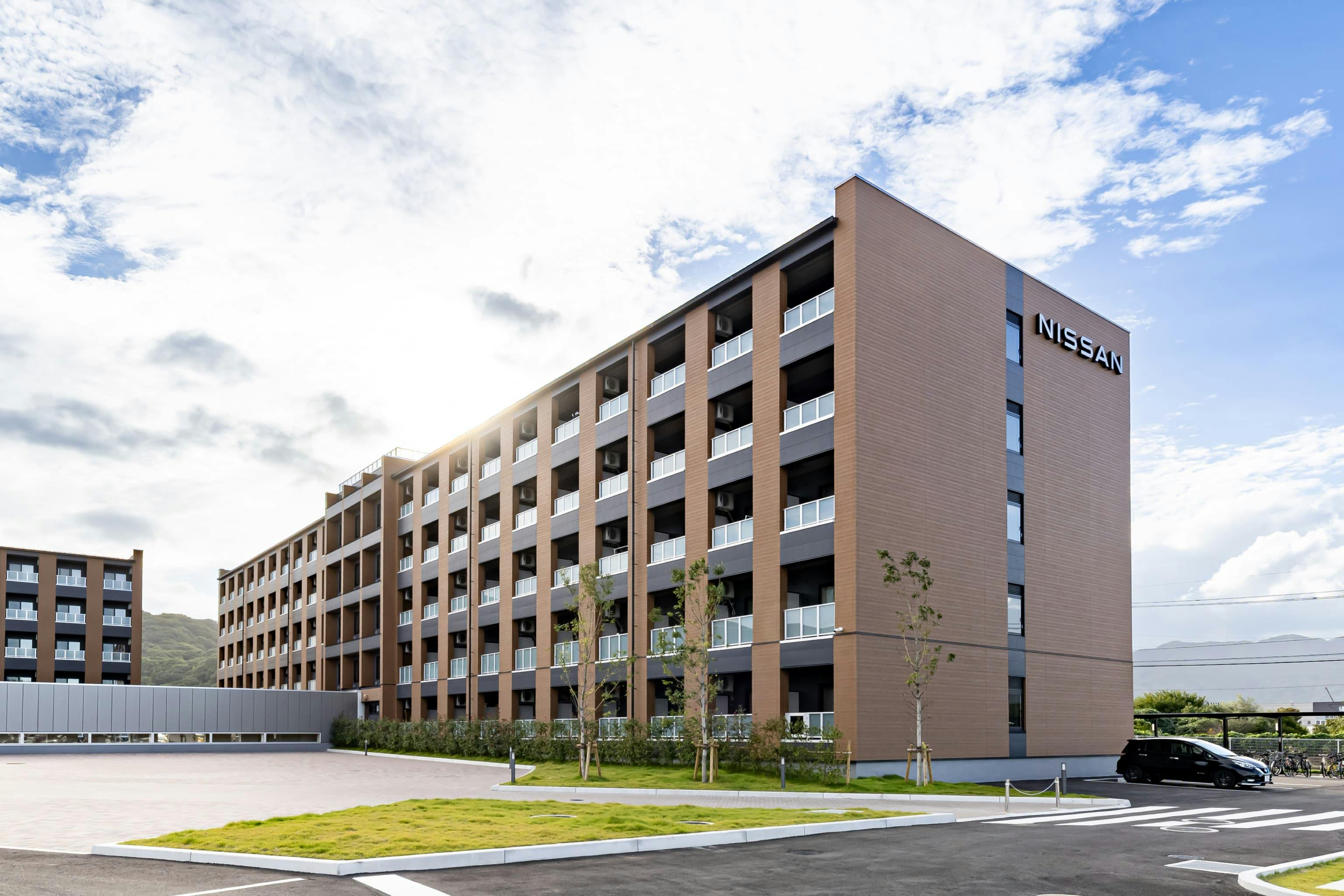 日産自動車九州株式会社 様の事例写真／[ドミトリー棟 外観]2〜5階の木造＋1階の鉄筋コンクリート造による、ハイブリッド構造のドミトリー棟。先進技術を扱う自動車メーカーとして、地産の木材利用によりカーボンニュートラルとサーキュラーエコノミーへの貢献を目指します。