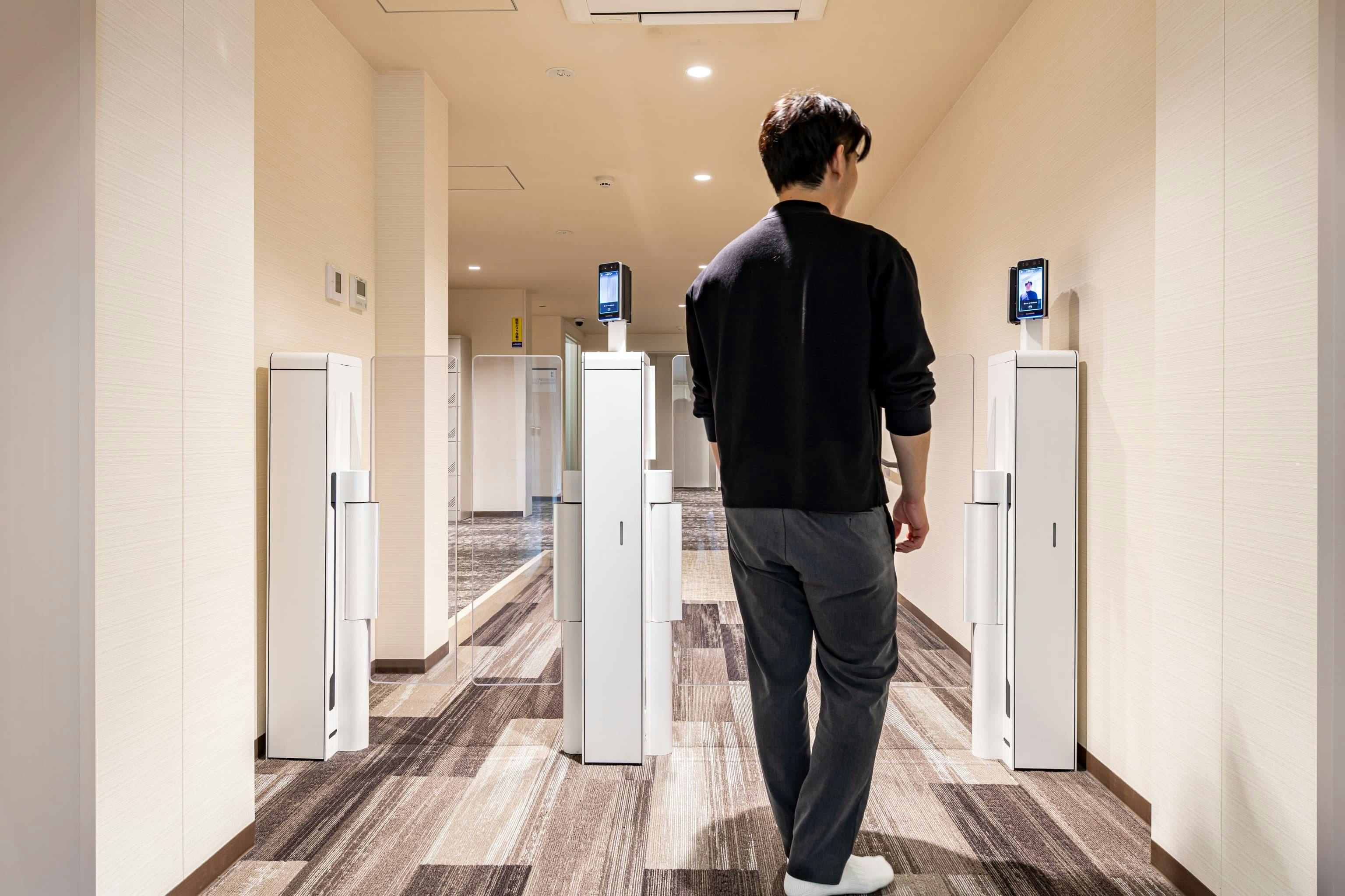 日産自動車九州株式会社 様の事例写真／[共用棟 1F ドミトリー棟へのエントランス]共用棟からドミトリー棟へと向かう通路には、顔認証によるセキュリティエントランスが設けられています。居住者以外の立ち入りを制限することで、日常の安全・安心を確保し、プライベートな空間を守っています。