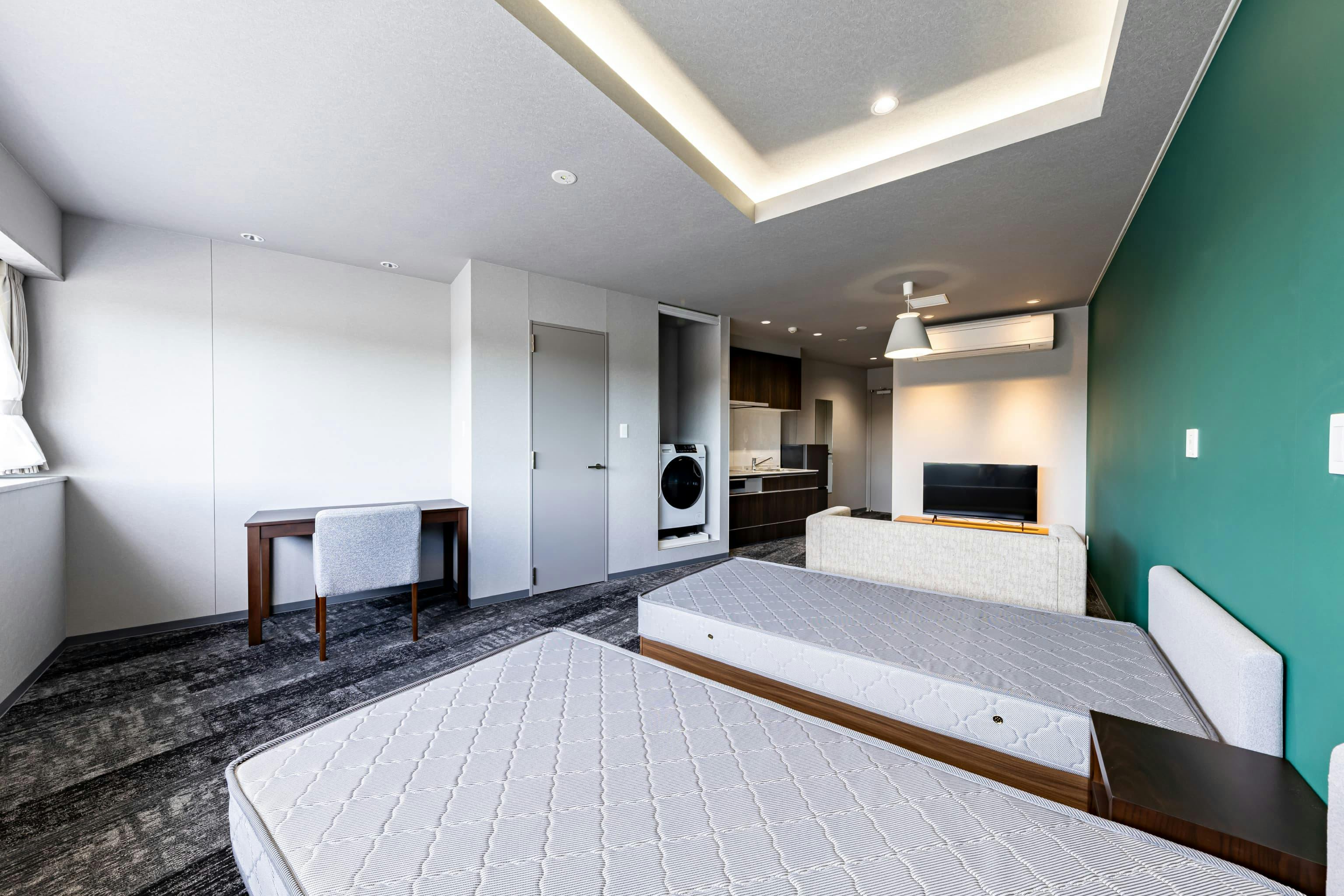 日産自動車九州株式会社 様の事例写真／[共用棟 2F ゲストルーム]入寮者以外はドミトリー棟に立ち入りができないため、家族など来客用にゲストルームが用意されています。ホテルライクな内装に、ベッドやキッチン、浴室・トイレ、洗濯機など、滞在に必要な機能が一通り整えられています。