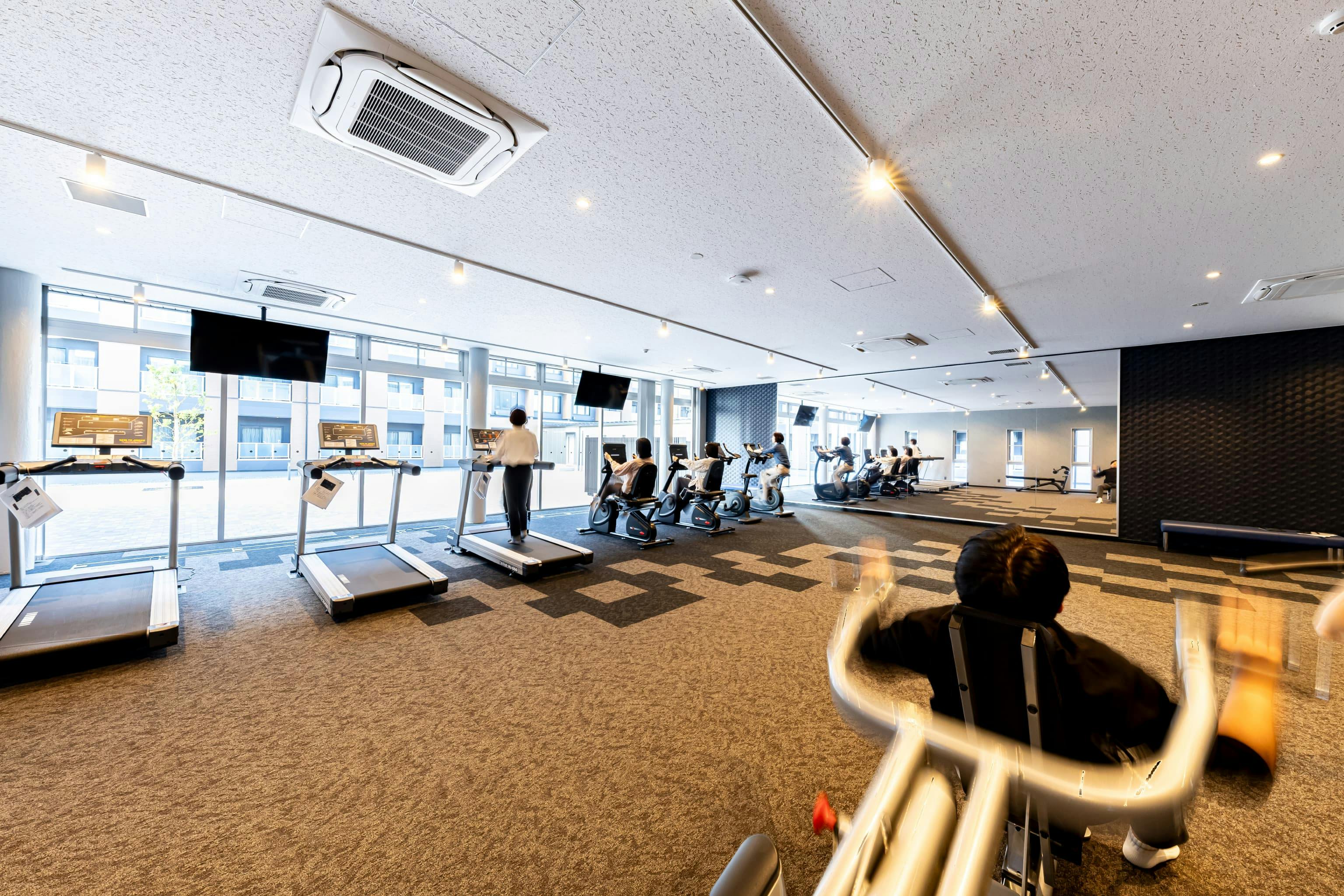 日産自動車九州株式会社 様の事例写真／[共用棟 1F ジム]最新のトレーニング機器とシャワーを備えたジムは、入寮者や社員から人気のスポット。日常的な運動を促し社員の健康を支えるほか、有事の際には地域住民の避難場所としても機能します。
