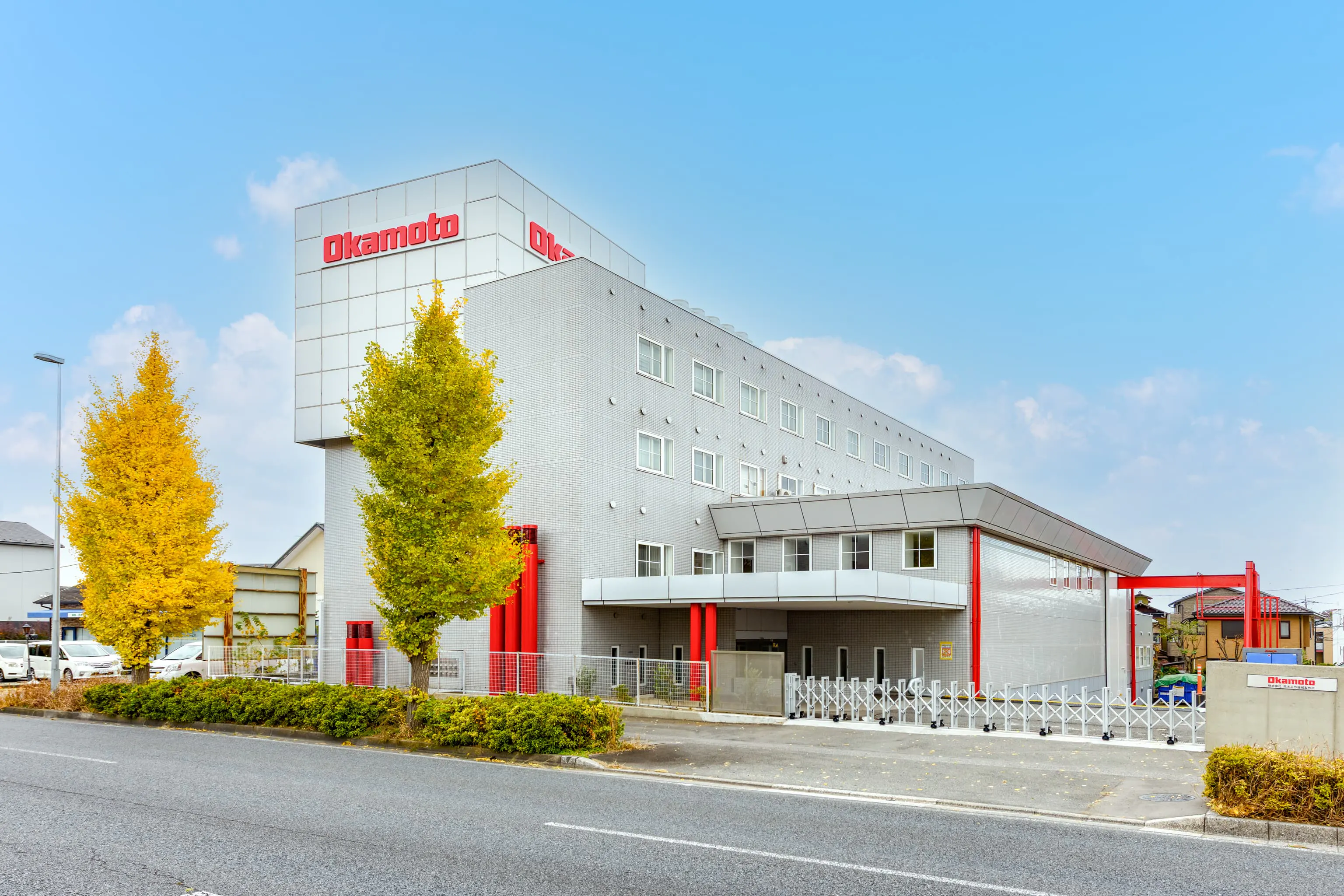 株式会社岡本工作機械製作所 様の事例写真／[外観]建物外観には社名ロゴを新設し、配管をコーポレートカラーの赤で塗装。既存ビルを活かしながら、企業らしさを印象づけるアクセントを加えています。
