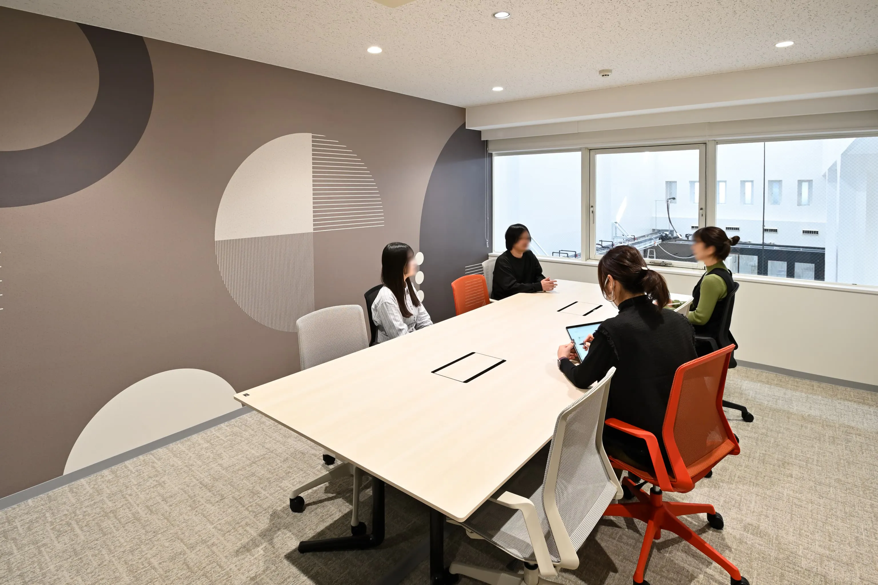 株式会社岡本工作機械製作所 様の事例写真／[1F会議室]各部屋で少しずつ壁面の色調を変えることで、空間にリズミカルな表情が添えられています。ウェハーと無限のつながりを象徴する円モチーフが企業のアイデンティティをさりげなく表現し、創造性を刺激します。