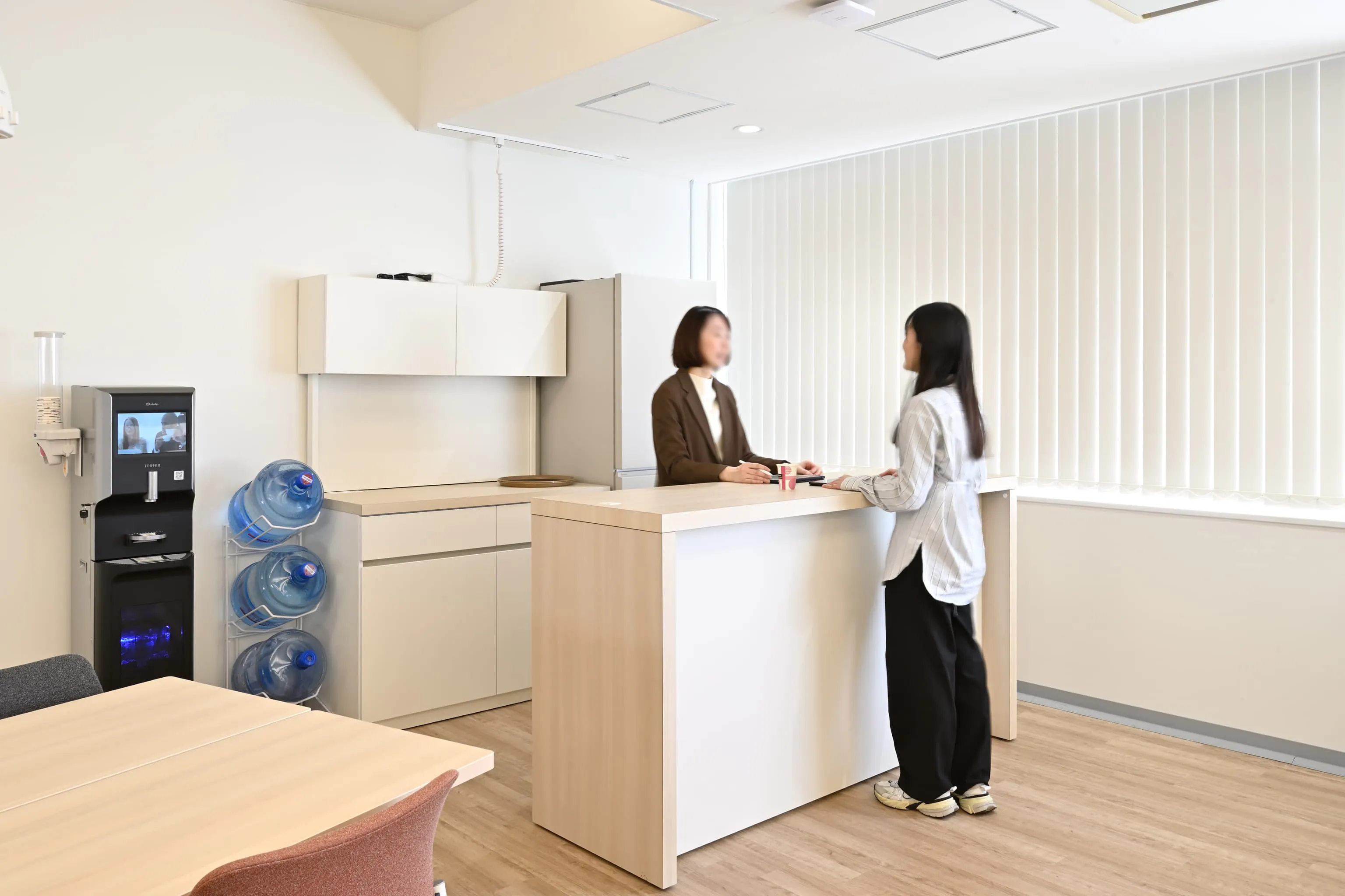 株式会社岡本工作機械製作所 様の事例写真／[2Fカフェ（コラボレーションエリア）]コラボレーションエリアの一角にあるカフェカウンターは、飲み物を取りに立ち寄る社員が磁石に引き寄せられるように自然と集まるマグネットスペースです。偶発的な会話が生まれ、交流を穏やかに広げています。