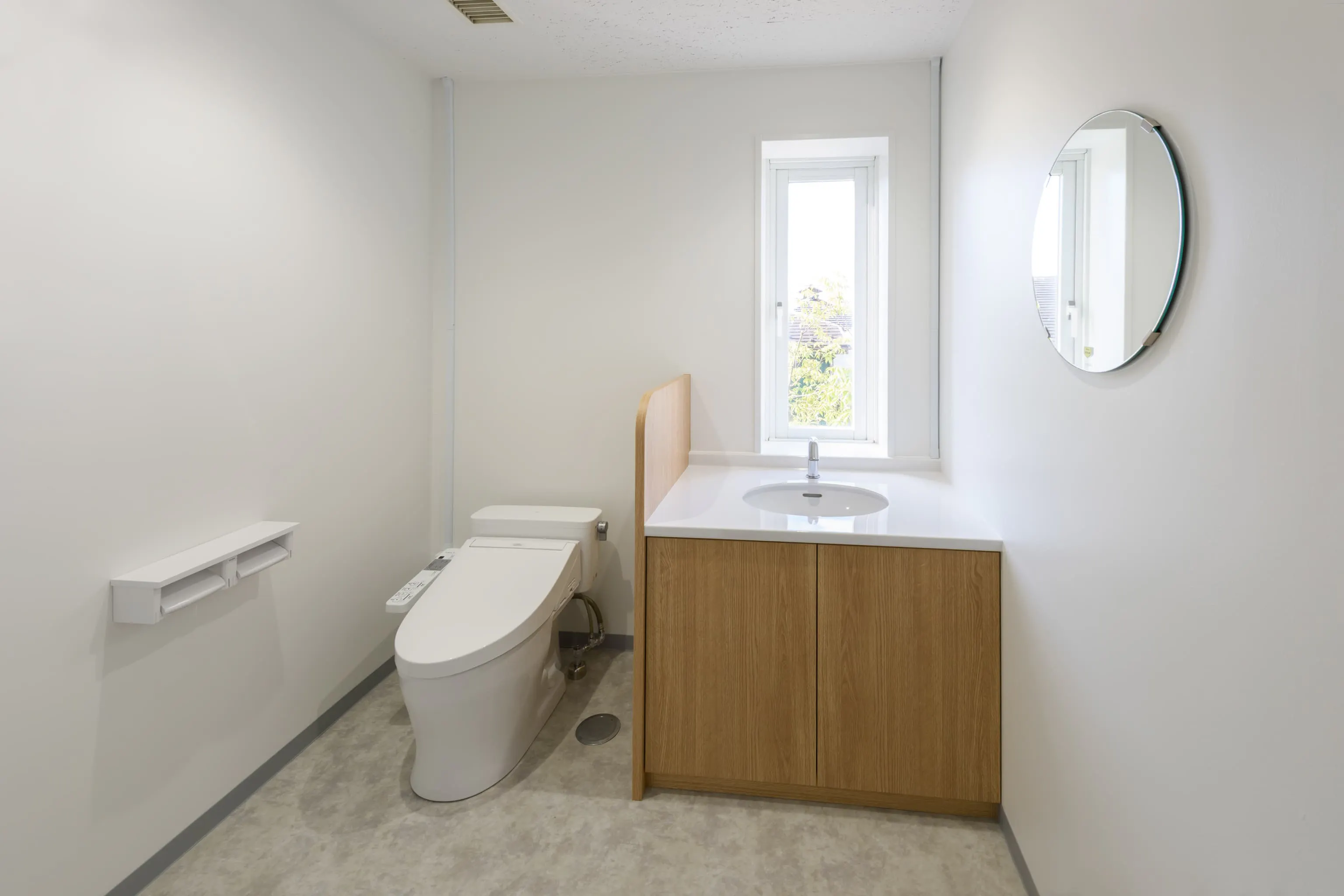 株式会社岡本工作機械製作所 様の事例写真／[２Fトイレ]2階トイレには円形ミラーを採用し、各所に展開されている「連続性・円」のモチーフをさりげなく取り入れました。日常的に利用する場所にも、空間全体と調和するデザインが息づいています。