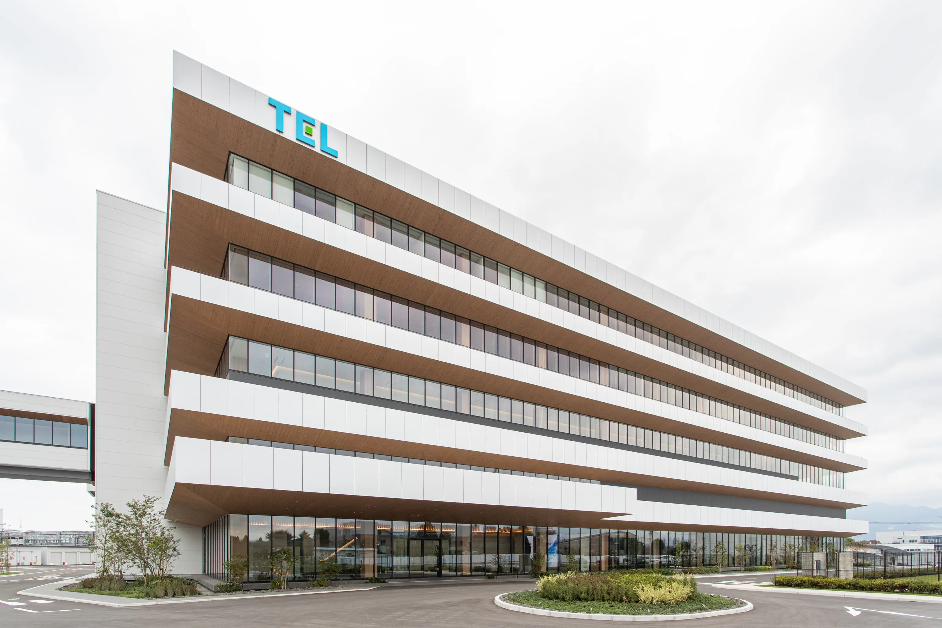 東京エレクトロン九州株式会社 様の事例写真／[プロセス開発棟の外観]「Ascending（上昇感）」をデザインコンセプトに設計された4階建てのプロセス開発棟は、2階の連絡通路で既存棟と行き来できます。オフィス内にたっぷりと陽光を取り込む、大きなガラス窓が印象的です。